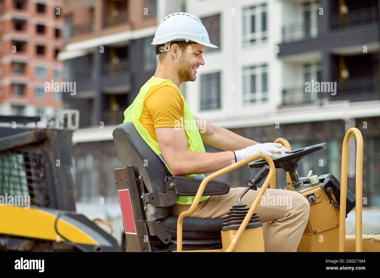 Joyeux homme en gants de coton conduisant une machine de compacteur de sol Banque D'Images