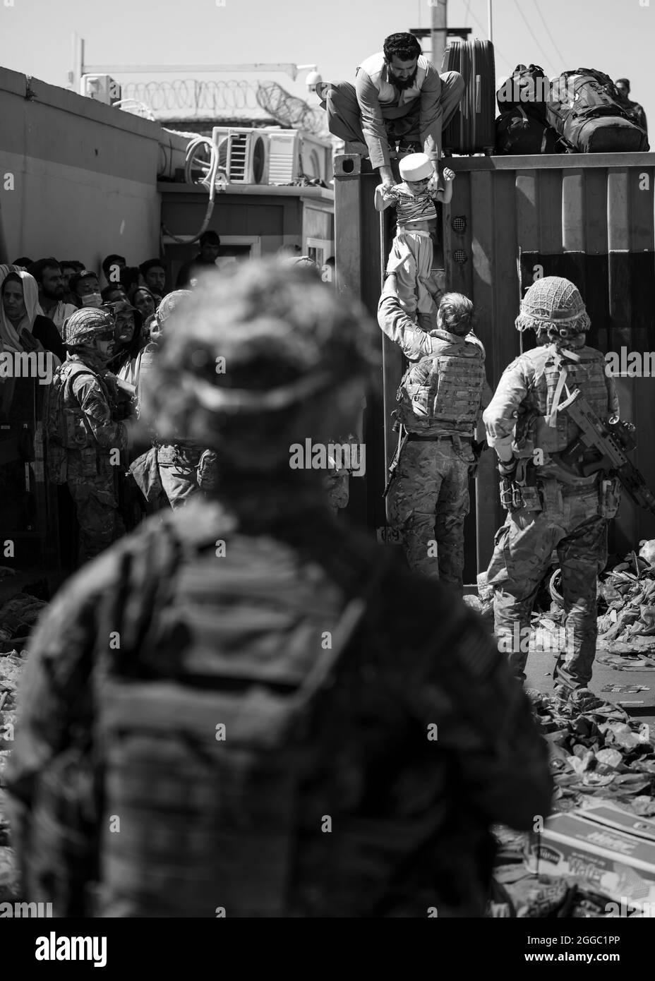 Un afghan remet son enfant à un parachutiste britannique affecté au 2e Bataillon du Régiment de parachutistes, tandis qu'un membre de la 1re Brigade combat Team, 82e Division aéroportée, assure la sécurité à l'aéroport international Hamid Karzaï de Kaboul, en Afghanistan, le 26 août 2021. Le 82e ABN. Le Div. Continue de faciliter l'évacuation en toute sécurité des citoyens américains, des demandeurs de visa d'immigrant spécial et des autres Afghans à risque hors d'Afghanistan le plus rapidement et en toute sécurité possible. (É.-U. Photo de courtoisie de l'armée) Banque D'Images