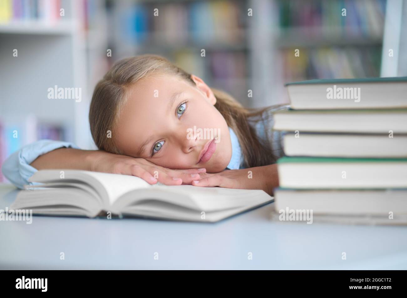 Un écolier épuisé allongé sur son manuel de bibliothèque Banque D'Images