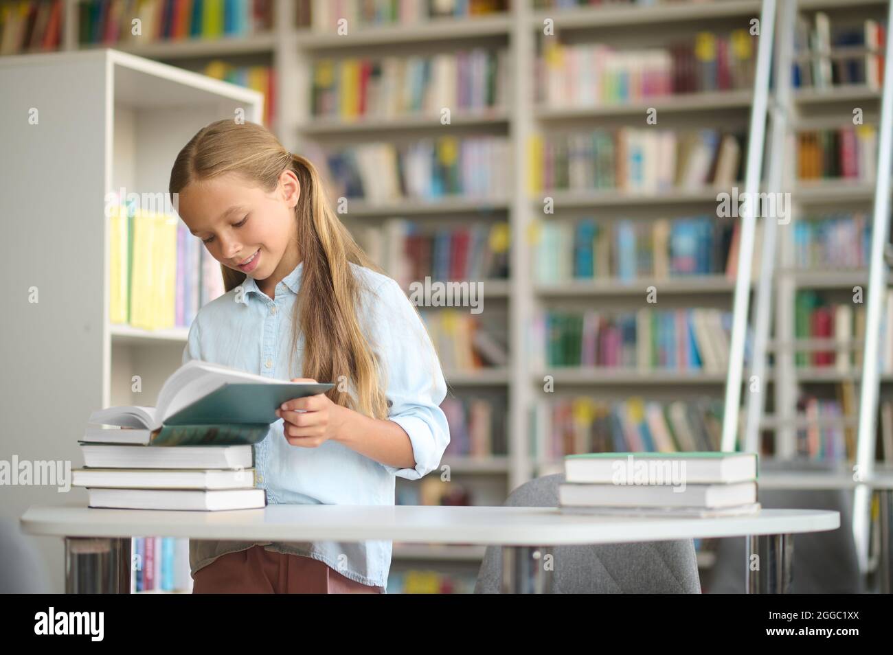 Un élève joyeux lisant un manuel au bureau de la bibliothèque Banque D'Images