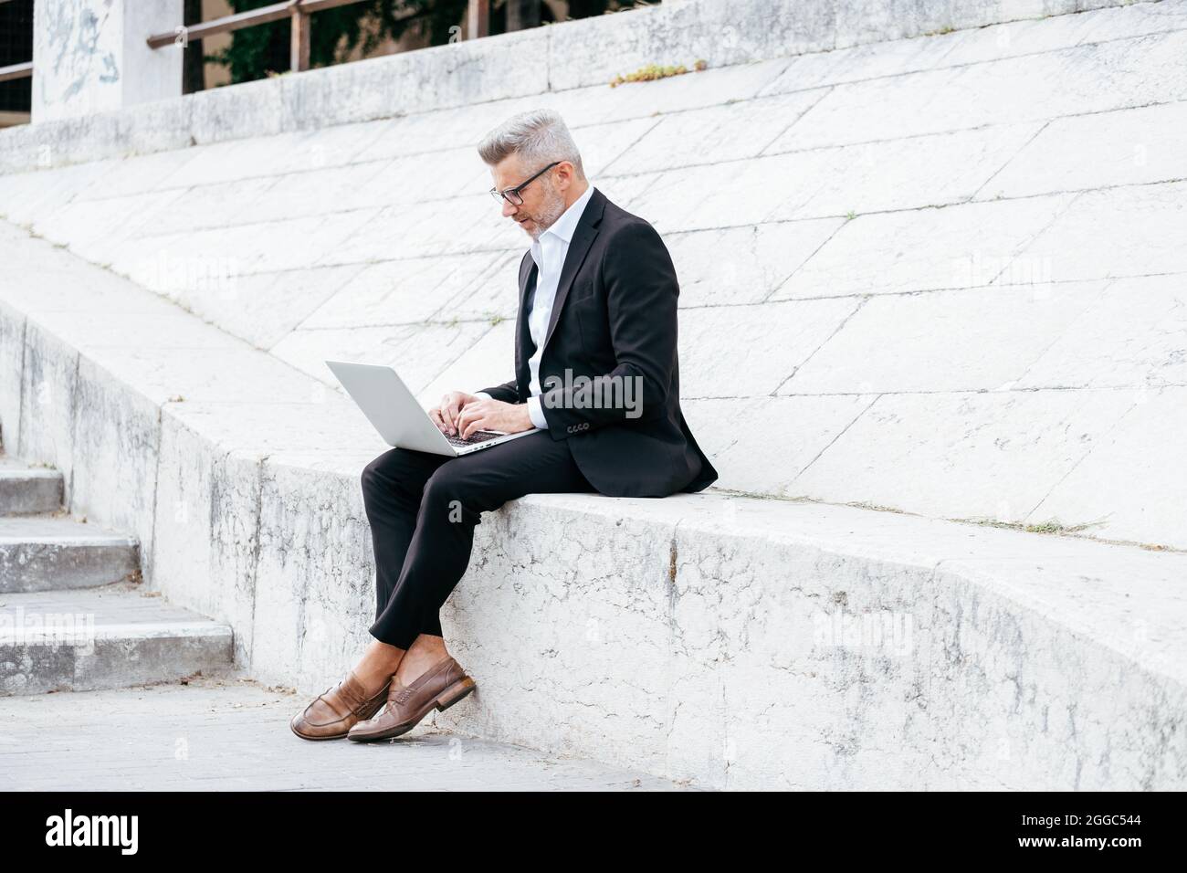 Homme d'affaires travaillant ordinateur portable tout en étant assis sur les escaliers dans le centre-ville Banque D'Images