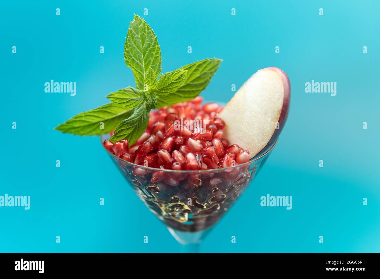Graines de grenade saines dans un verre à cocktail avec pomme et menthe sur fond bleu Banque D'Images