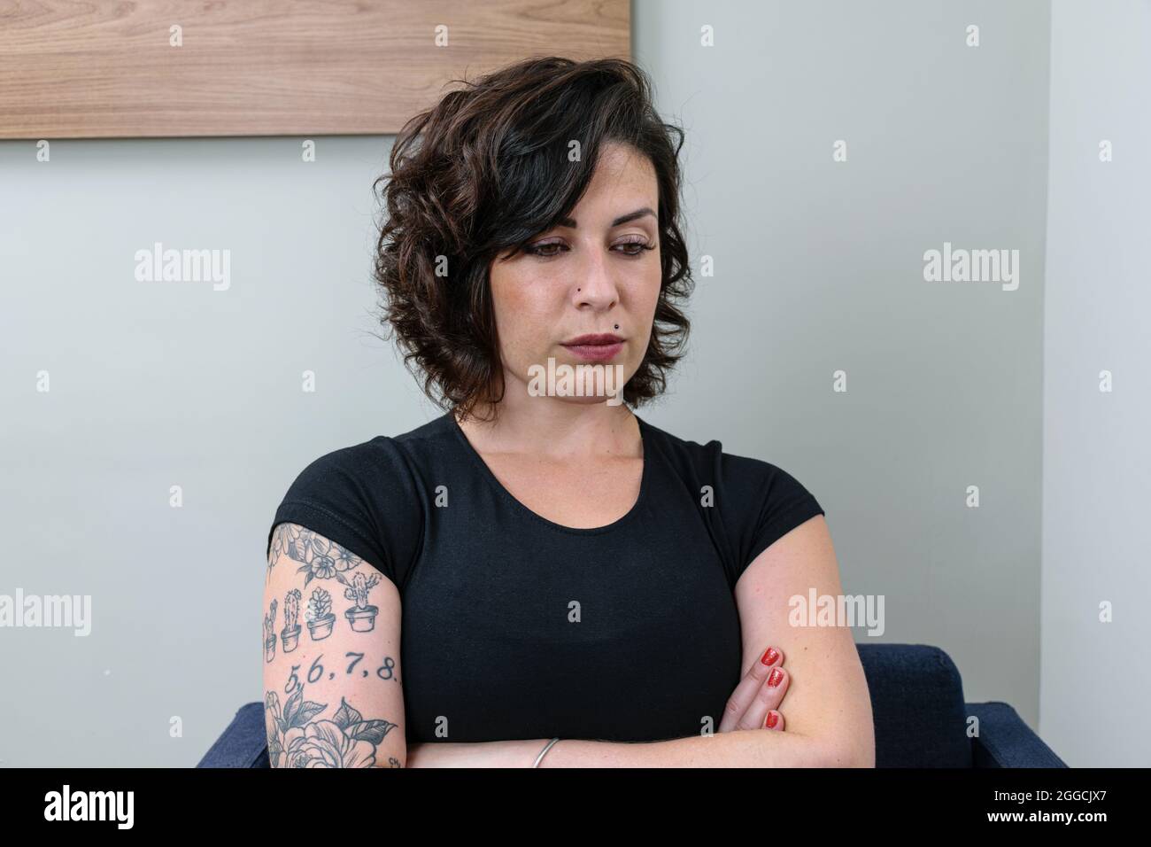 Femme brésilienne, tatouée, avec les bras croisés et regardant vers le bas. Réfléchi et contrarié. Banque D'Images