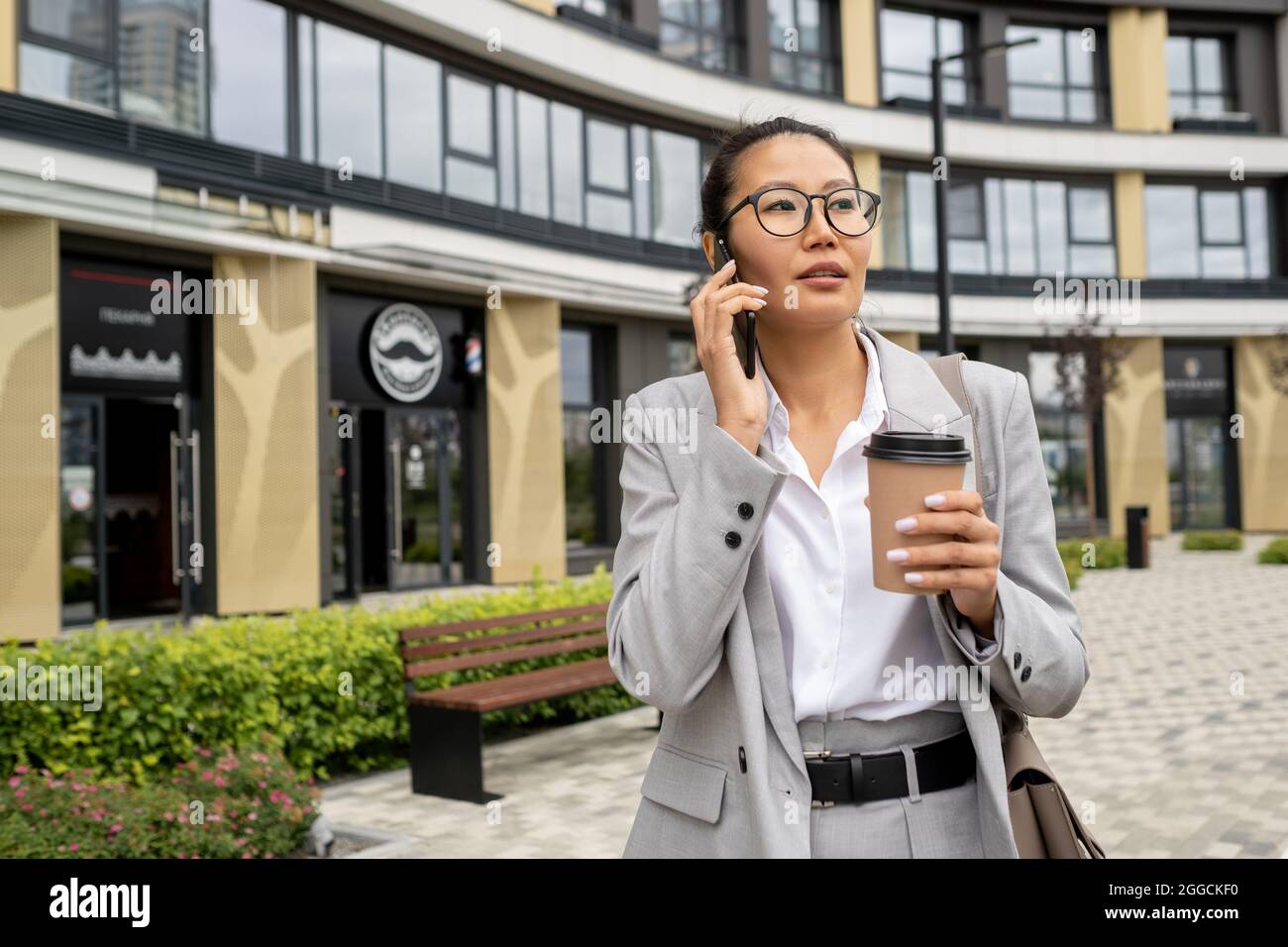 Jeune femme d'affaires confiante avec un smartphone à l'oreille prenant un verre à l'extérieur Banque D'Images