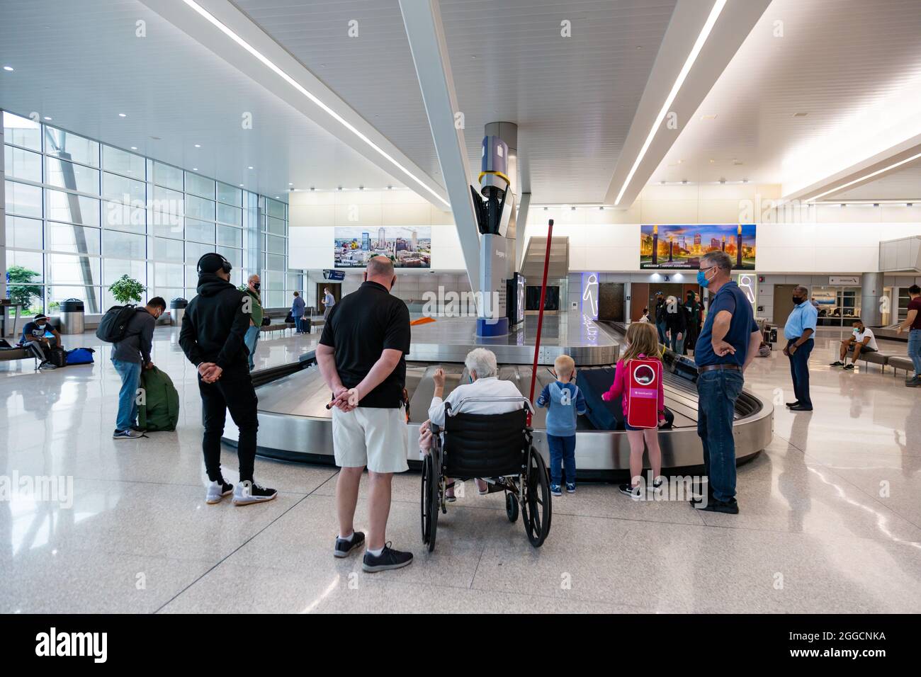 Une femme handicapée attend dans son fauteuil roulant ses bagages aux côtés d'autres voyageurs à l'aéroport international d'Indianapolis retrait des bagages à Indy. Banque D'Images