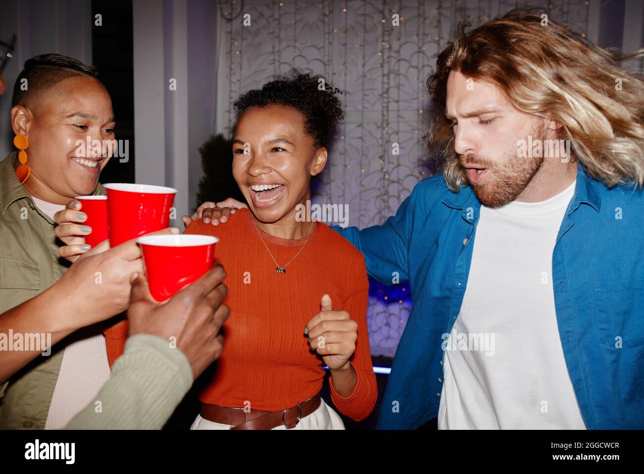 Divers groupes de jeunes amis qui profitent de la fête à l'intérieur et tiennent des tasses rouges, prises avec flash Banque D'Images