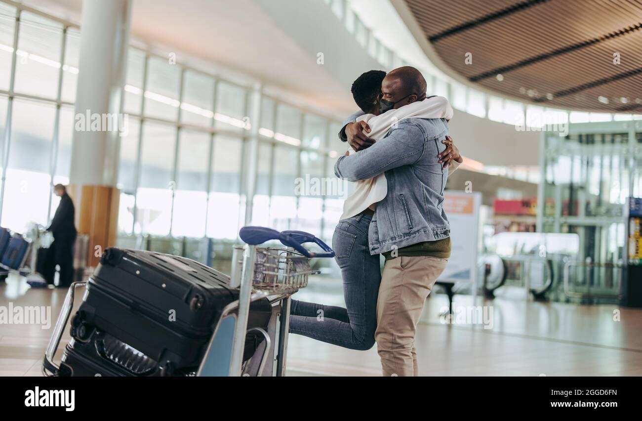 Homme avec masque embrassant et soulevant sa femme au terminal de  l'aéroport. Un homme africain rencontre une femme arrivant à l'aéroport  Photo Stock - Alamy