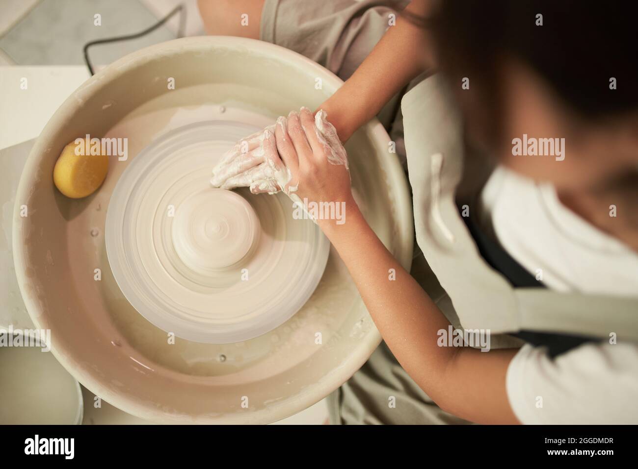 Vue de dessus de la femelle anonyme potter sculptant le clayware sur la roue de rotation pendant le travail dans l'atelier professionnel Banque D'Images