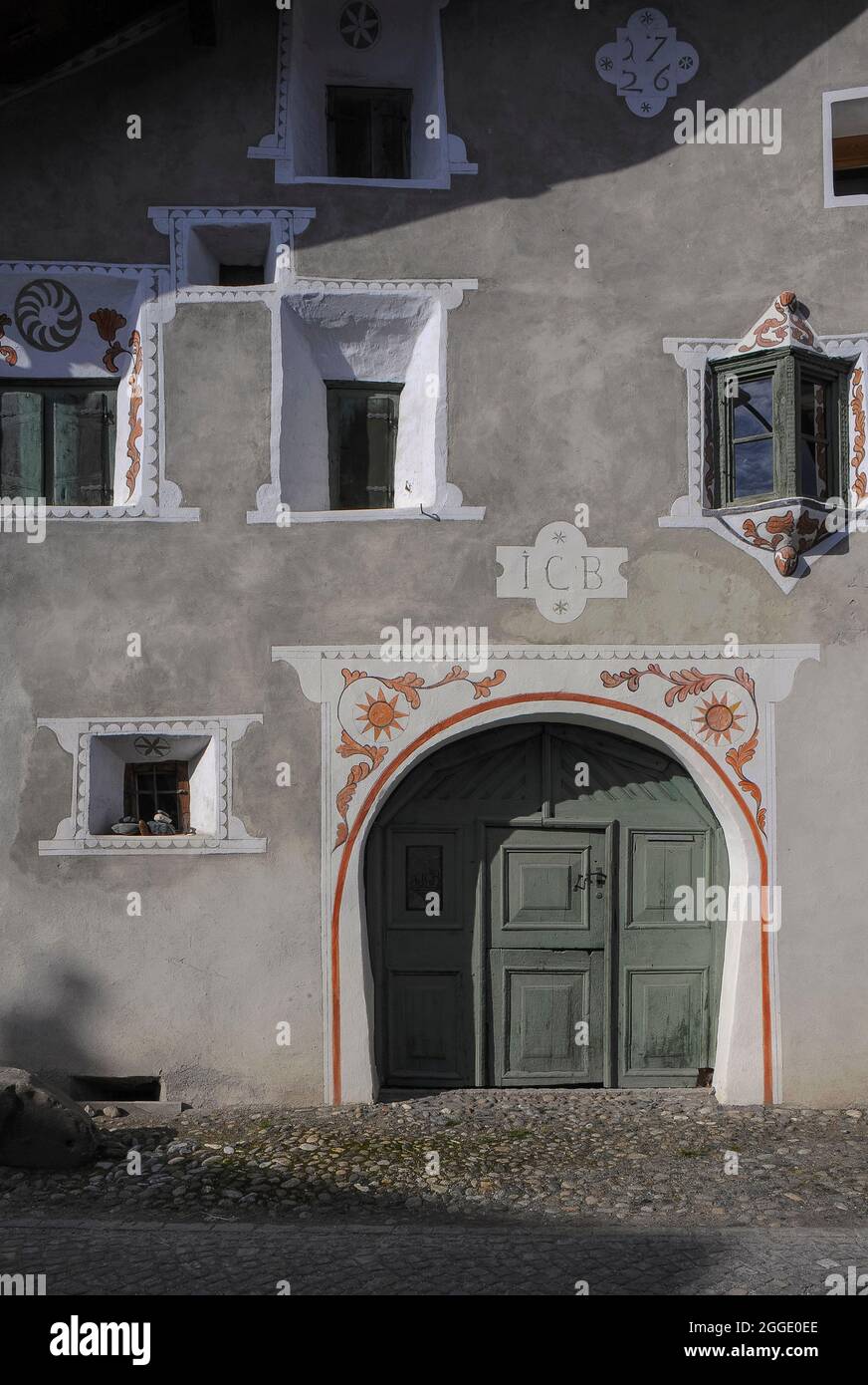 La décoration en sgraffite blanc avec des détails peints en orange complète les boiseries vertes de la porte de l'écurie à la maison restaurée de Scuol, Graubünden ou canton des Grisons, Suisse. La maison, datée de 1726, dispose d'un double aspect «balcun tort» ou fenêtre oriel (à droite), également peinte en vert. « Balcun tort » est un terme romanche et ces fenêtres sont typiques de la région romanche de Suisse. Banque D'Images