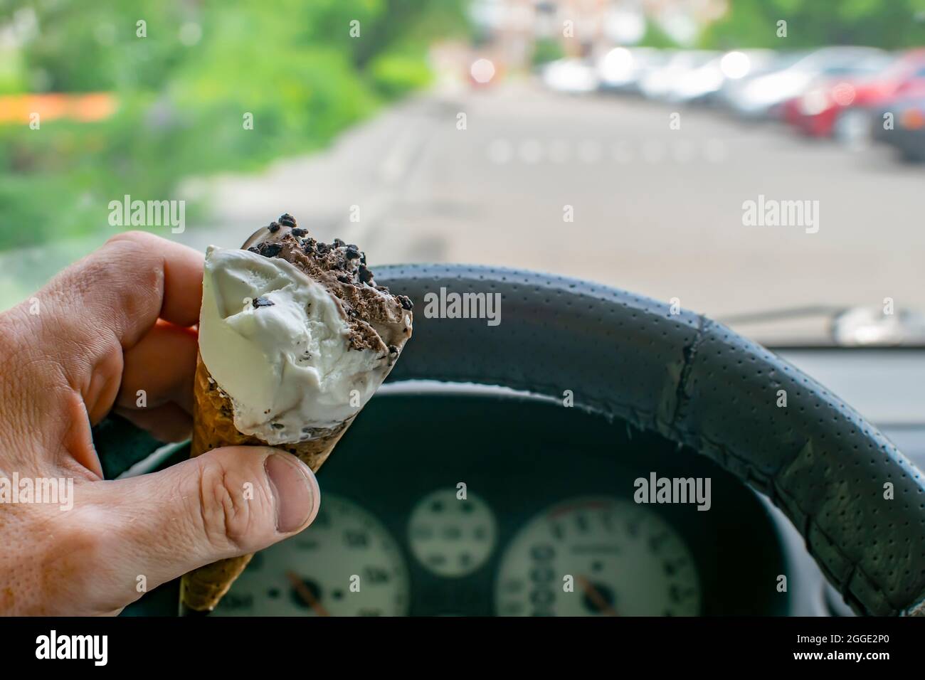 grignotez du chocolat et de la crème glacée au lait dans une tasse à gaufres comestibles dans la main du conducteur à l'intérieur de la voiture à l'heure du déjeuner tout en attendant par temps chaud et ensoleillé Banque D'Images