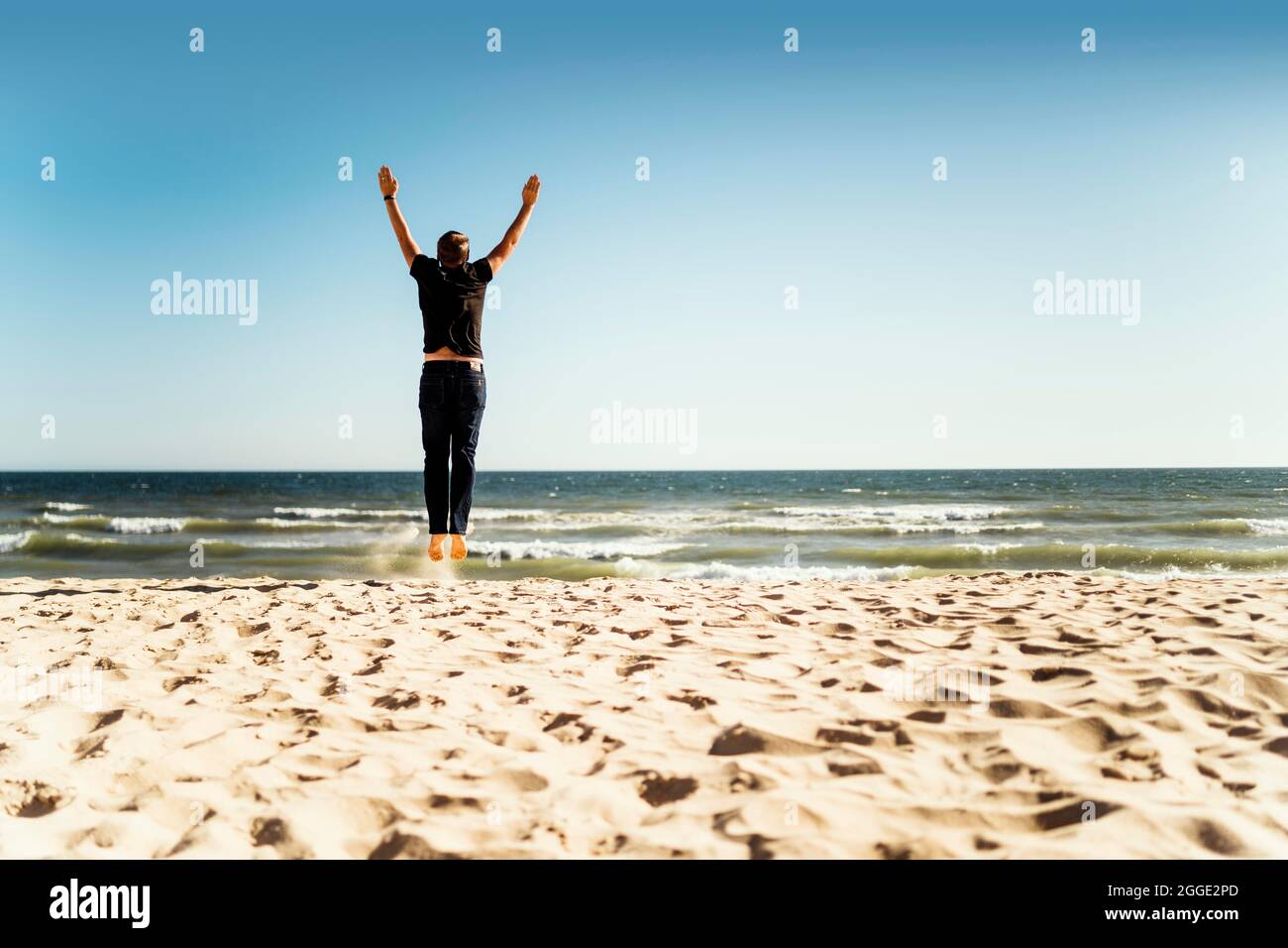 Homme sautant sur la plage avec les mains levées Banque D'Images