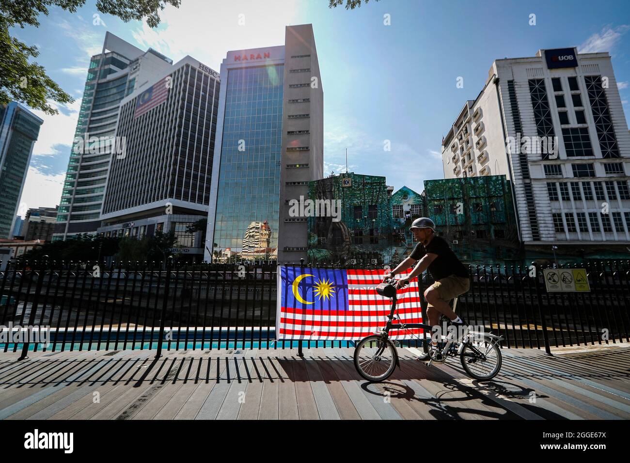 Un cycliste passe devant un drapeau malaisien lors des célébrations de la 64e journée nationale à Kuala Lumpur.la Malaisie célèbre chaque année son 64ème jour de l'indépendance le 31 août, elle commémore la Déclaration d'indépendance de Malaisie du 31 août 1957. Banque D'Images