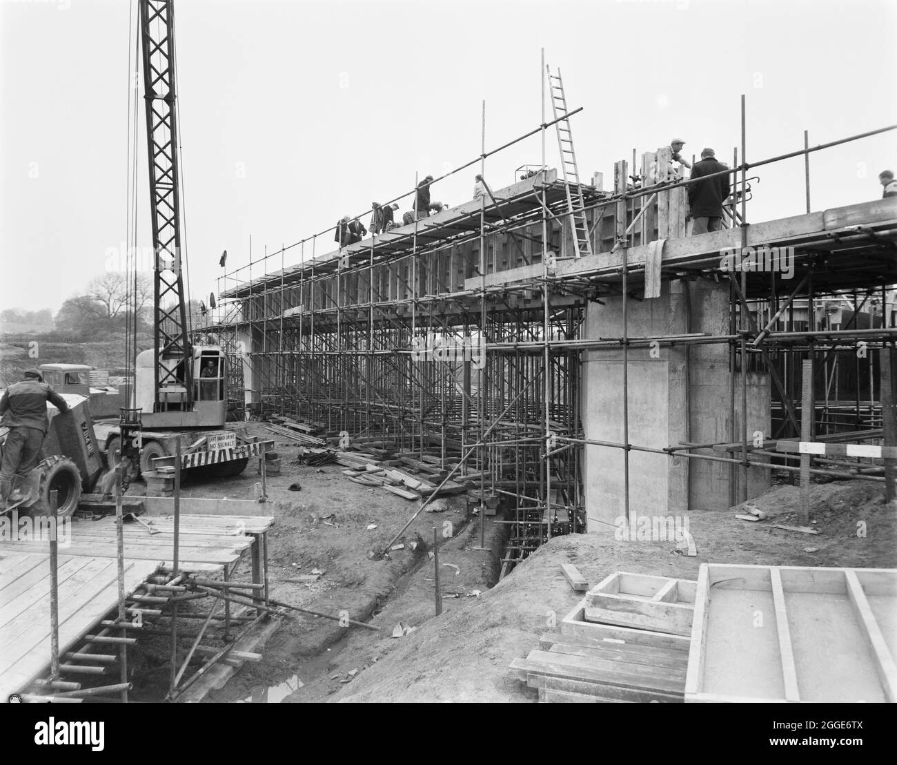 Vue de la construction de l'autoroute Birmingham-Preston (M6), montrant la première des grandes poutres post-tensionnées concrétisées in situ sur le pont 306 (pont Barn Bank Lane). Dans l'album, la légende dactylographiée ci-dessous la photo indique "béton étant placé à la première des grandes poutres post-tendues de 95'-0" de long, 70 tonnes sur le pont 306/ (Barn Bank Lane). Ceux-ci sont coulés sur les butées et les jetées en raison des difficultés de manipulation des poutres de cette taille. Ce faisceau particulier a maintenant été soumis à des contraintes et est auto-soutenu sur toute la plage. » Ce pont routier, qui est situé Banque D'Images