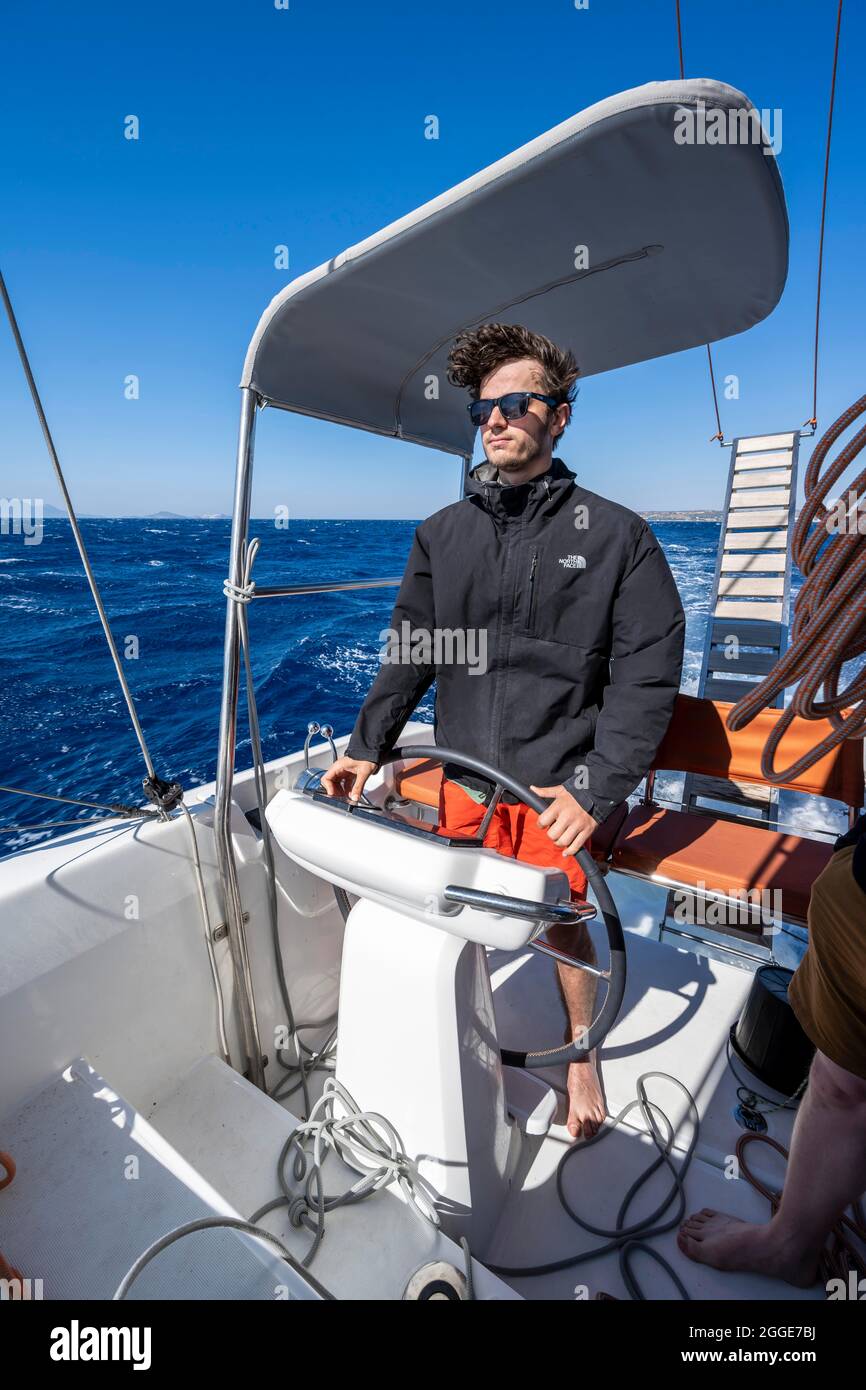 Homme au volant dans le cockpit sur le pont d'un catamaran, voyage en voilier, Dodécanèse, Grèce Banque D'Images