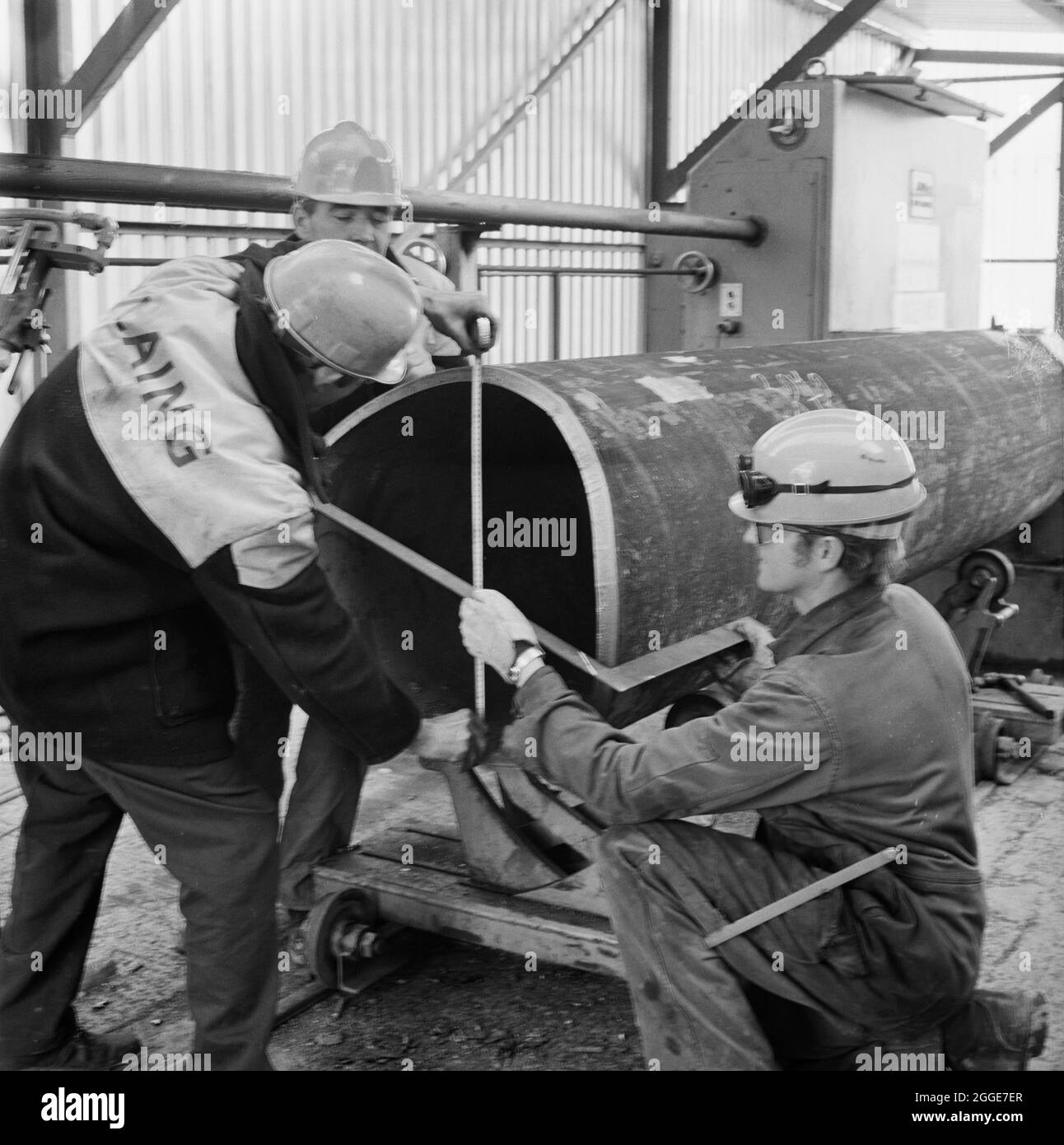 Une équipe de travailleurs de Laing mesurant un grand tube métallique dans l'un des huttes de soudage de Graythorp. Au début des années 1970, Laing pipelines Offshore a construit le chantier de fabrication Graythorp et le quai sec sur le site de l'ancien chantier naval William Gray. L'entreprise a créé un quai sec qui a été utilisé pour la construction de plates-formes fixes de forage en mer du Nord pour le projet pétrolier BP en mer du Nord. En 1972, un millier d'hommes travaillaient sur place pour construire une structure tubulaire qui soumettrait un engin de forage en mer du Nord destiné à l'Oilfield des Forties. Banque D'Images