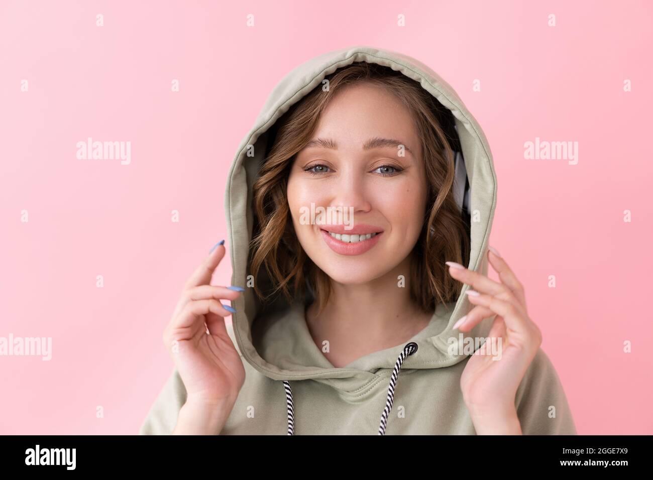 Happy dents sourire femme tient le capot avec ses mains caucasienne femme aiment habillé grand hoodie rose fond gros portrait Banque D'Images