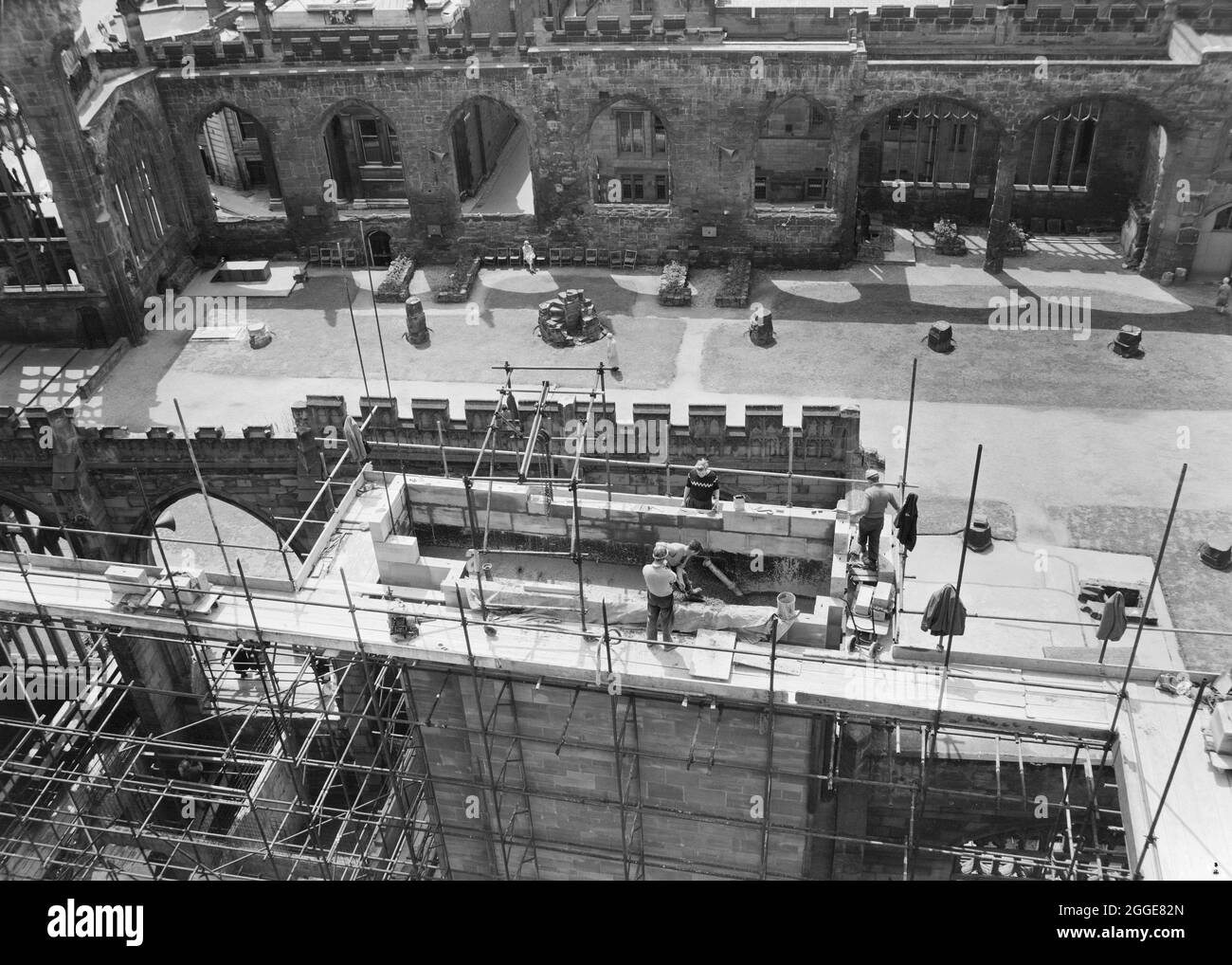 Une vue des constructeurs travaillant au sommet de l'échafaudage sur la construction de la cathédrale de Coventry, avec les ruines de l'ancienne cathédrale derrière. La photo montre la construction de la nouvelle cathédrale de Coventry, conçue par Basil Spence en 1951 et construite entre le milieu des années 1950 et 1962. Il a remplacé l'église de la cathédrale Saint-Michel en ruines qui avait été gravement endommagée par les bombardements en 1941. Banque D'Images