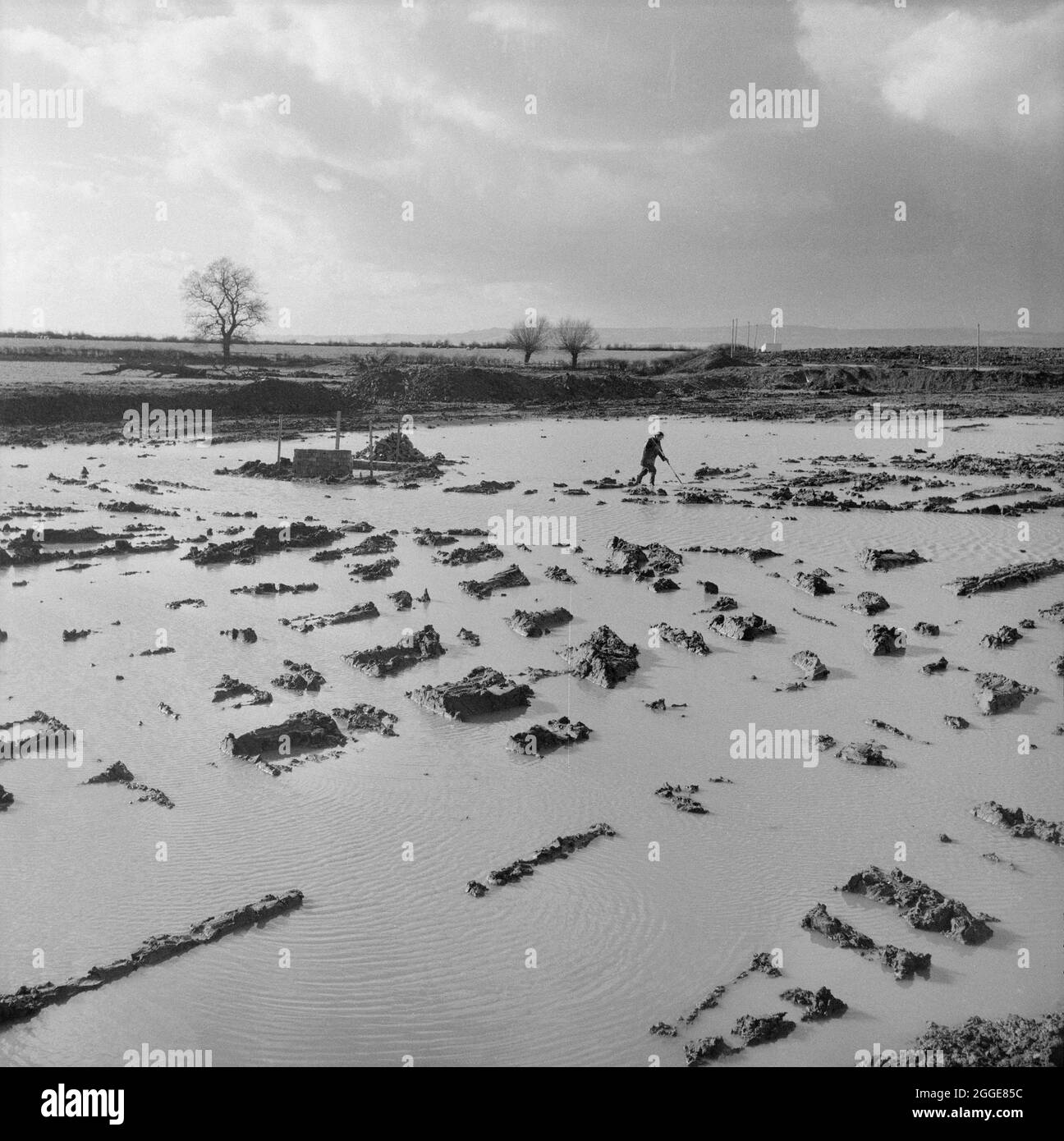 Vue sur une zone inondée du site de construction de la centrale nucléaire de Berkeley, montrant une figure effectuant une base de contrôle sur le périmètre du site après une pluie nocturne. Cette image a été cataloguée dans le cadre du projet Breaking New Ground en partenariat avec la John Laing Charitable Trust en 2019-20. Banque D'Images