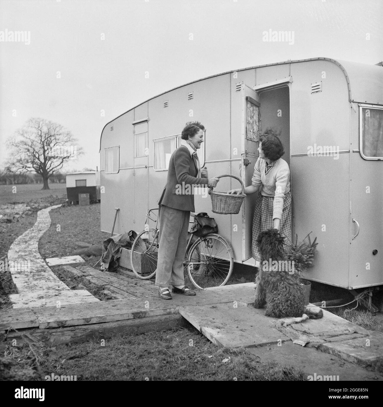 L'épouse du boucher local livrant des fournitures à Mme Glover, vivant dans une caravane sur un site temporaire à la centrale nucléaire de Berkeley pendant sa construction. La centrale nucléaire de Berkeley a été la première centrale nucléaire commerciale au Royaume-Uni et l'une des premières générations de réacteurs nucléaires en Grande-Bretagne. Laing était les ingénieurs civils pour le projet, les travaux commençant le 7 janvier 1957. Le site de 57 acres comprenait des bureaux et des logements temporaires avec des installations pour les travailleurs sur le site. Mme Glover, montrée dans la photographie, était l'épouse de Jim Glover qui était un RI de pelle de Lima Banque D'Images