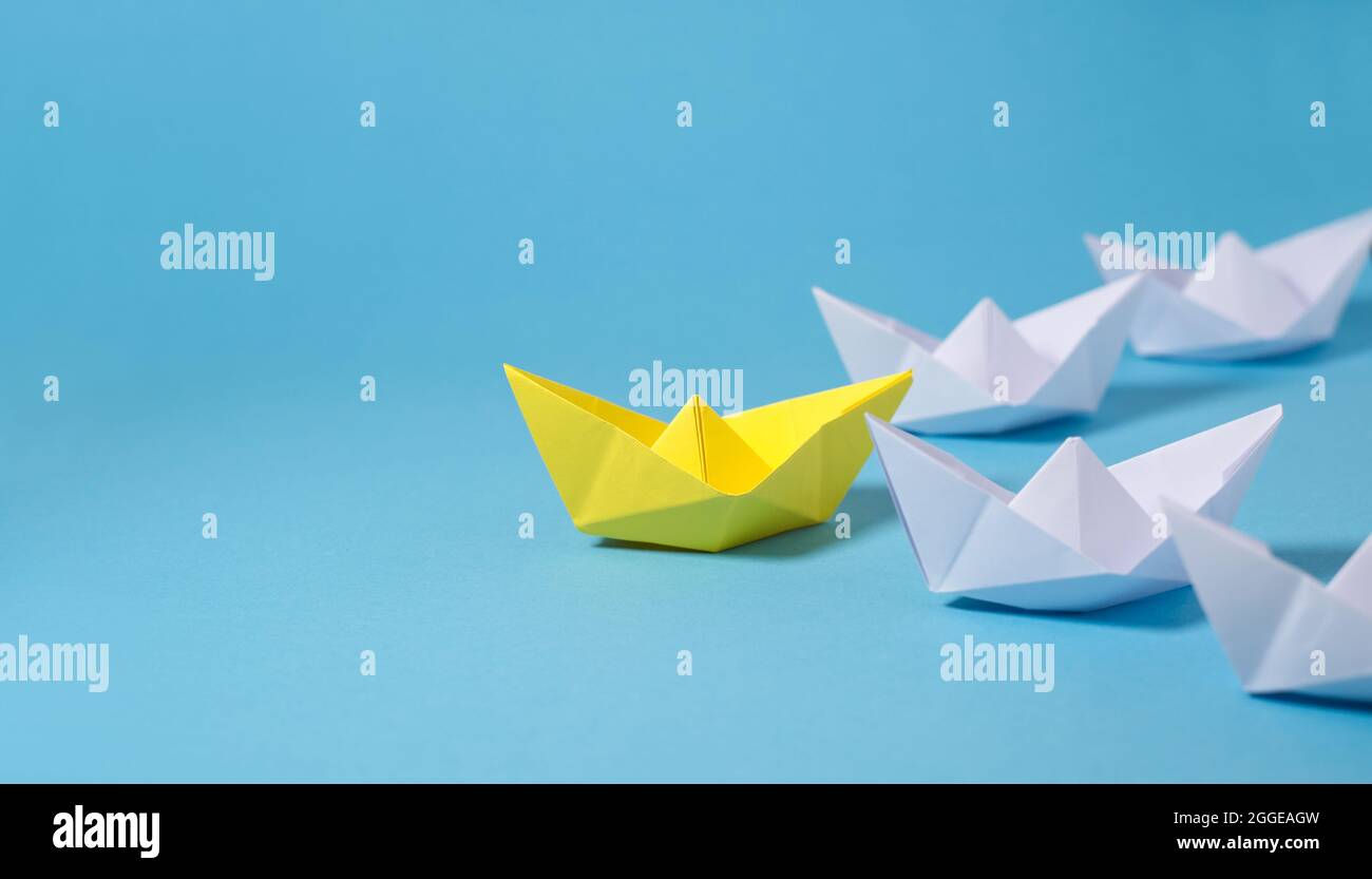 Concept d'entreprise de leadership avec un bateau à papier de leader jaune qui mène parmi les blancs sur fond bleu avec espace de copie. Banque D'Images