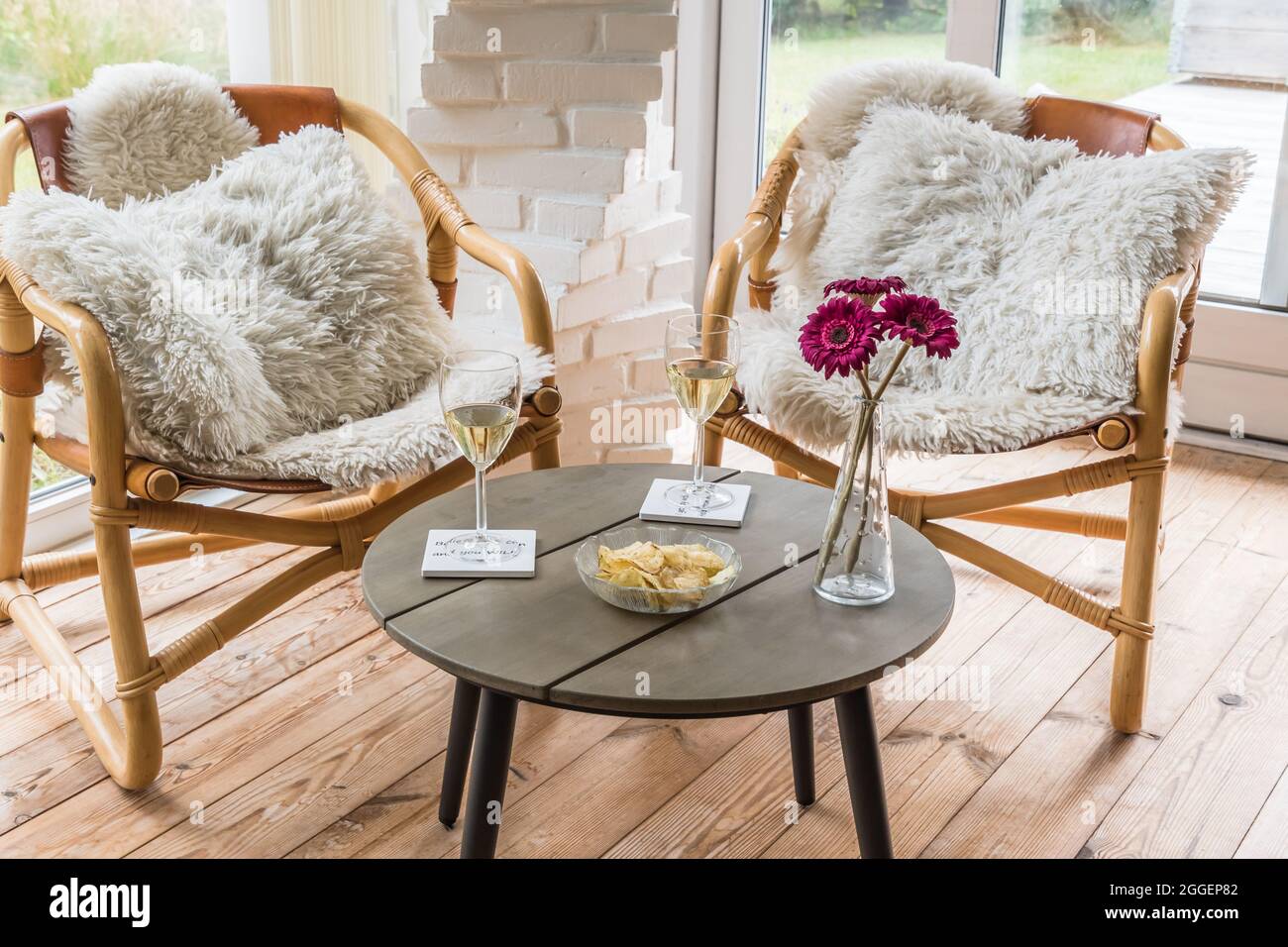 Deux chaises en osier avec oreillers et table basse avec verres à vin et en-cas dans un jardin d'hiver Banque D'Images