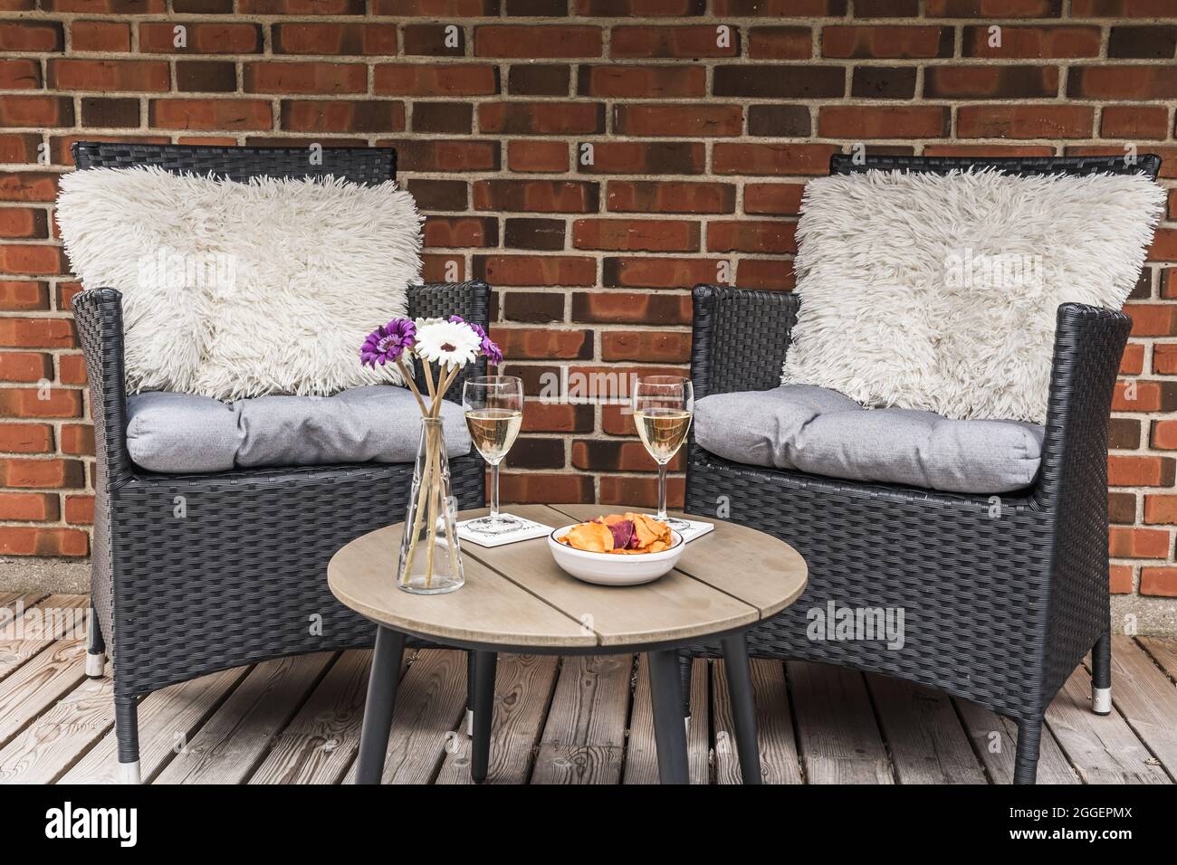 Deux chaises en rotin avec coussins et une petite table avec verres à vin sur une terrasse en bois, mur en pierre en arrière-plan Banque D'Images