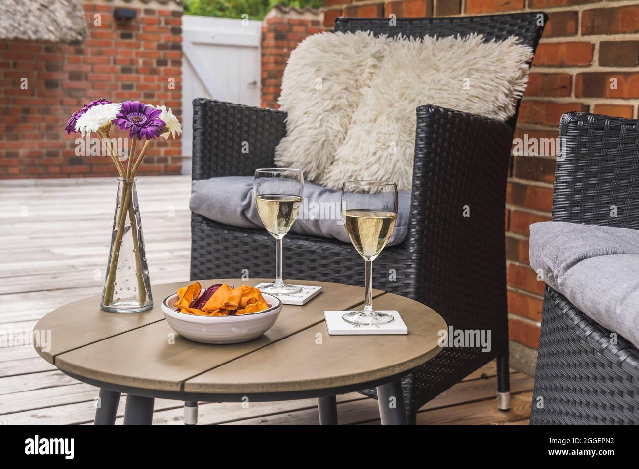 Chaise en rotin avec coussins et petite table avec verres à vin sur une terrasse en bois, mur en pierre à l'arrière-plan Banque D'Images