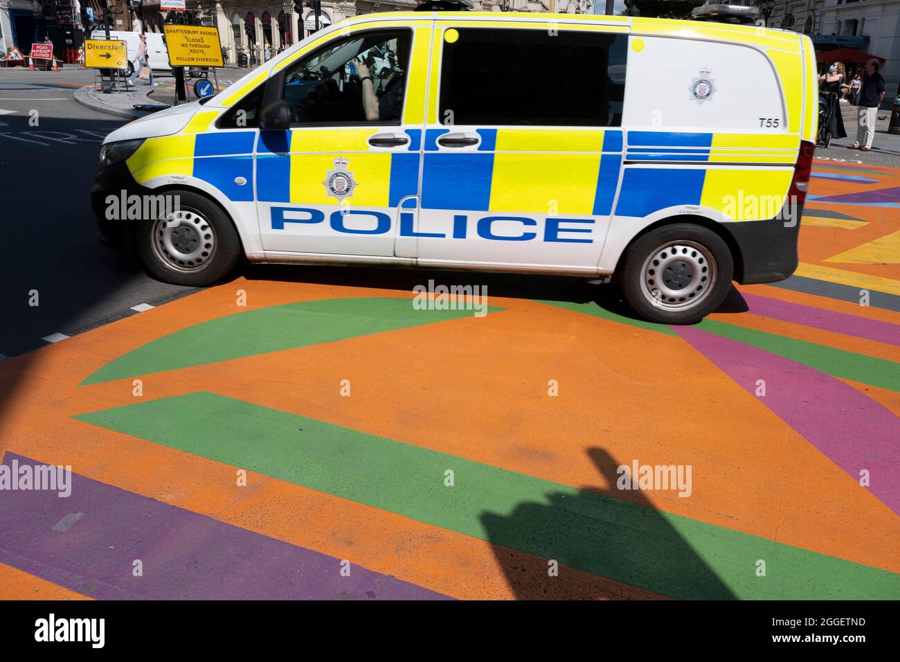 Une fourgonnette de police à la décoration bleue et jaune passe au-dessus des nouveaux passages pour piétons multicolores à motifs et graphiques à Piccadilly Circus le 10 août 2021 à Londres, au Royaume-Uni. Banque D'Images