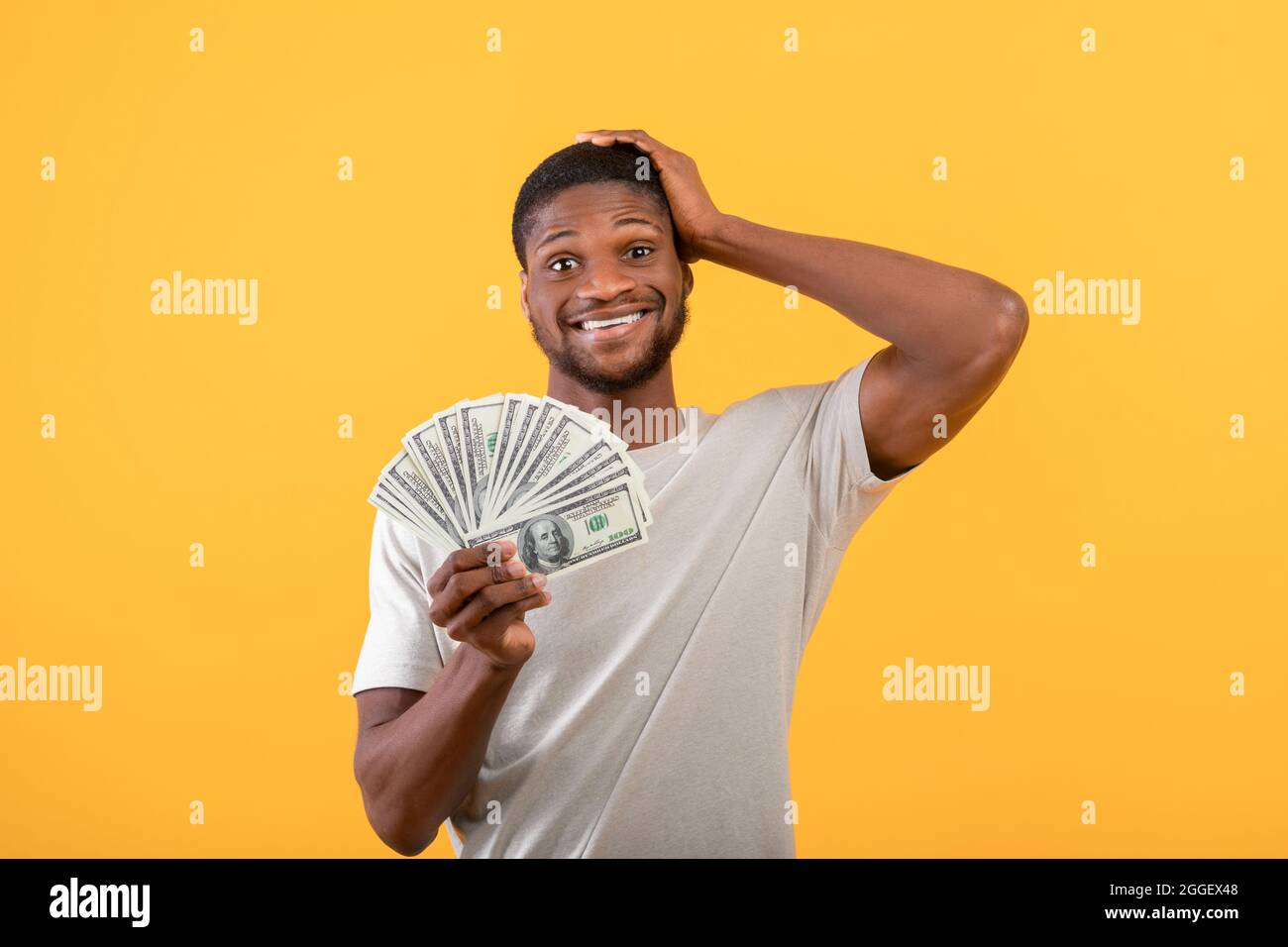 Grande chance et profit. Un homme noir choqué détenant beaucoup d'argent, ne peut pas croire sa grande victoire sur fond de studio jaune. Homme afro-américain avec poupée Banque D'Images