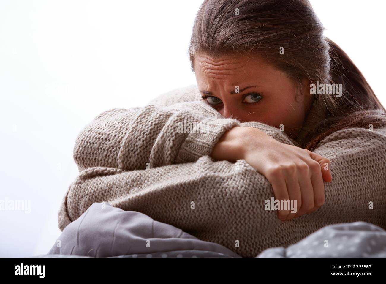 Une jeune femme troublée ou malade cache son visage dans son bras en regardant l'appareil photo avec des yeux larges et une fronde dans un portrait de gros plan court Banque D'Images