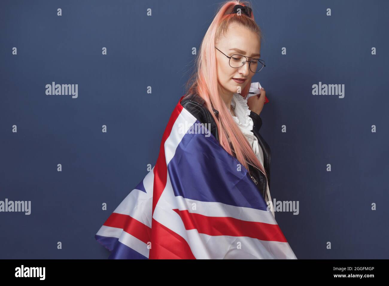 Jeune femme expatrié à lunettes avec le drapeau de la Grande-bretagne. Prise de vue en studio. Enseignant de hippster anglais. Fashionly habit la femme avec des poils roses en noir Banque D'Images