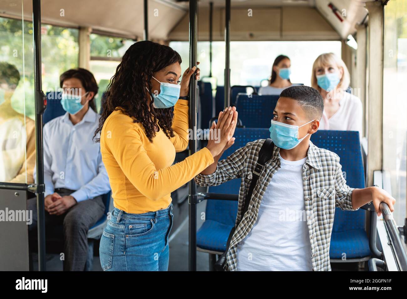 Portrait d'une heureuse mère afro-américaine qui parle à son fils et donne cinq hauts en se déplaçant en bus après l'école et en portant des masques pour le CO Banque D'Images