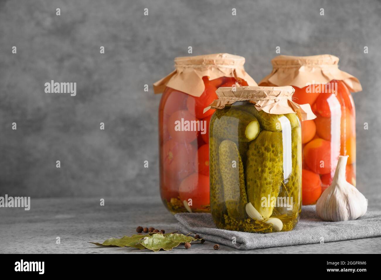 Tomates marinées et concombres faits maison. Légumes en conserve dans des pots en verre sur table grise. Copier l'espace. Récolte d'automne et préparatifs. Banque D'Images