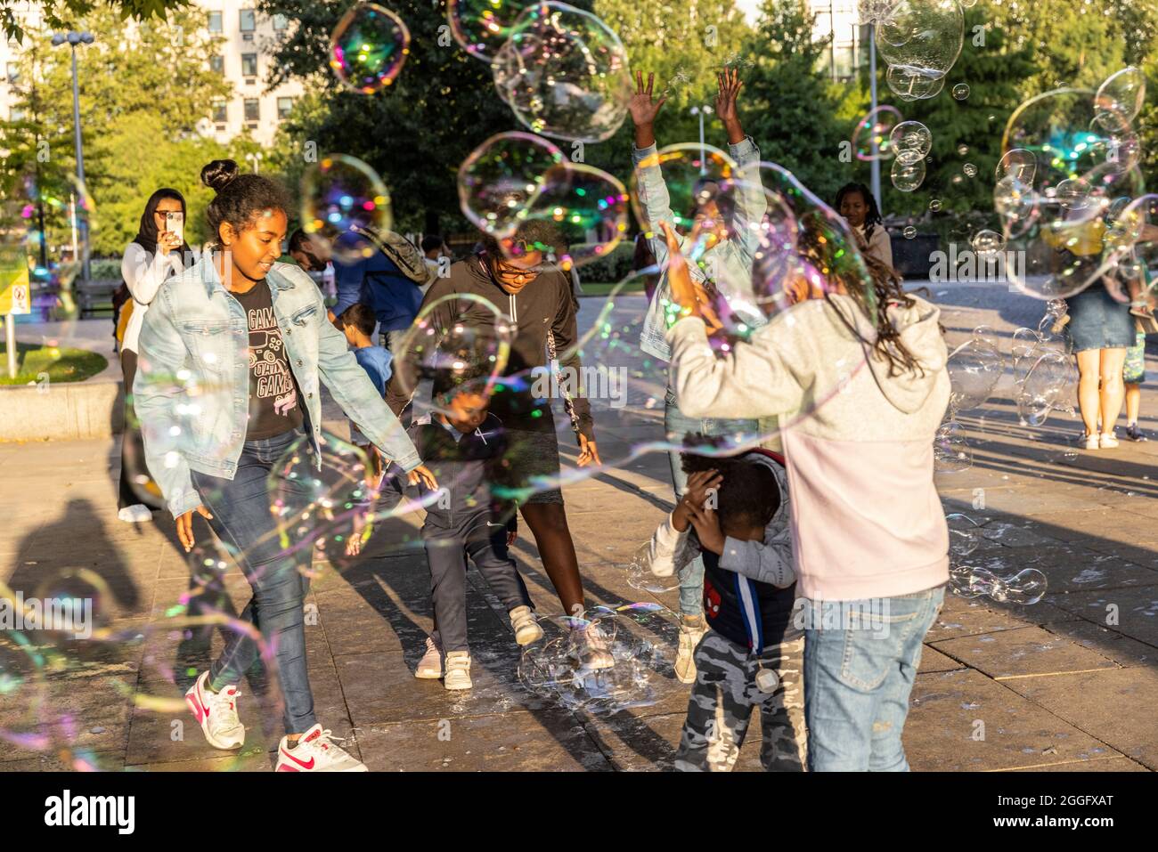 Les familles apprécient les divertissements de la rue le long de la Southbank à Londres tandis qu'un interprète souffle de grandes bulles à travers le pavé, Angleterre, Royaume-Uni. Banque D'Images
