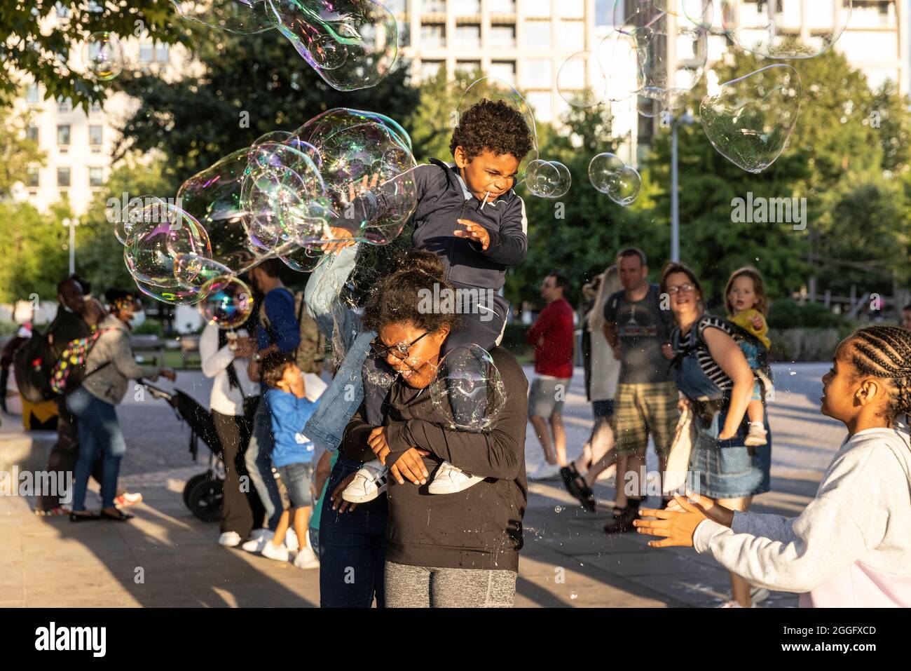 Les familles apprécient les divertissements de la rue le long de la Southbank à Londres tandis qu'un interprète souffle de grandes bulles à travers le pavé, Angleterre, Royaume-Uni. Banque D'Images