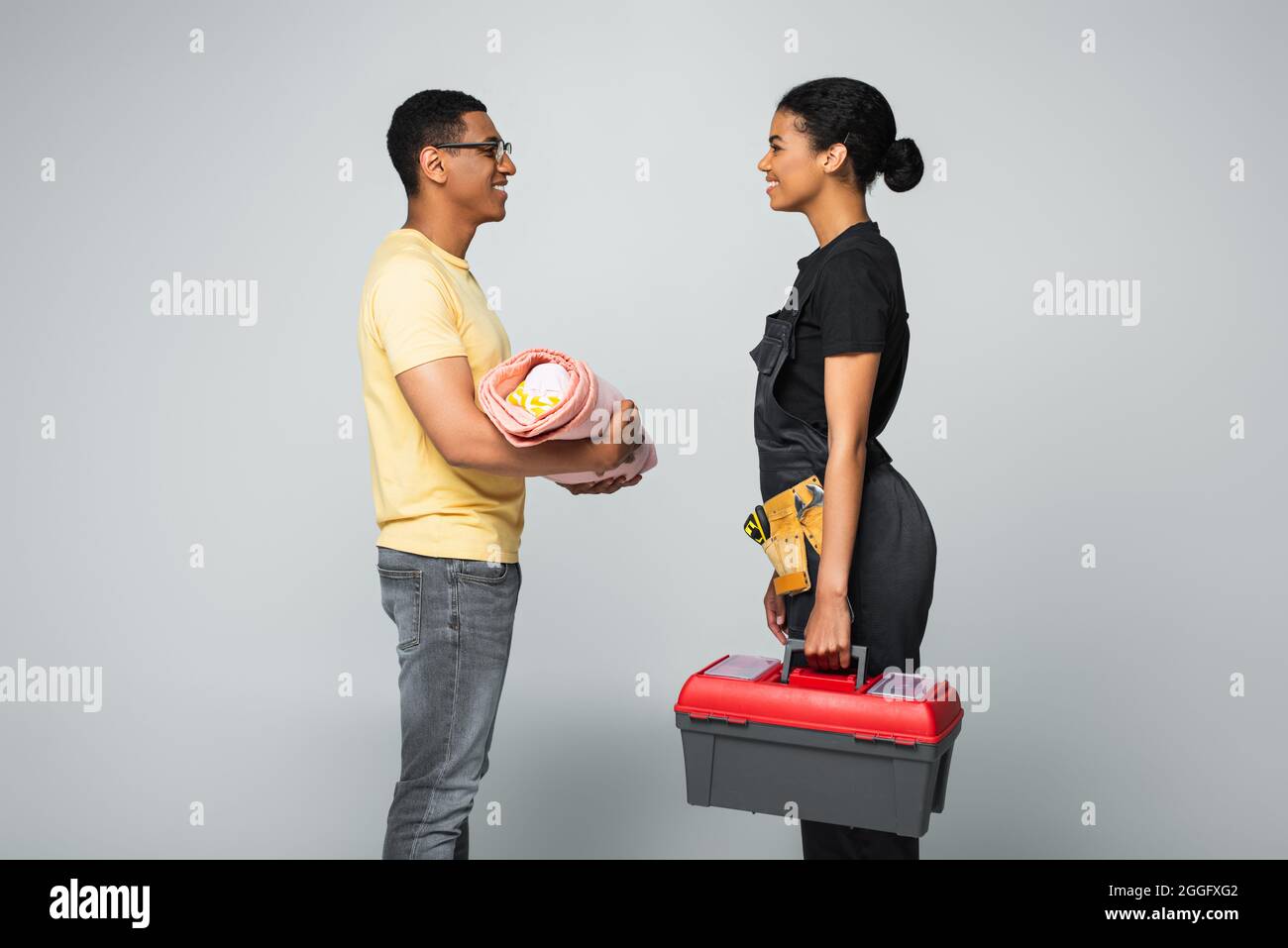 vue latérale d'un père afro-américain tenant un bébé recouvert d'une couverture près d'une femme de réparation avec boîte à outils sur le gris Banque D'Images