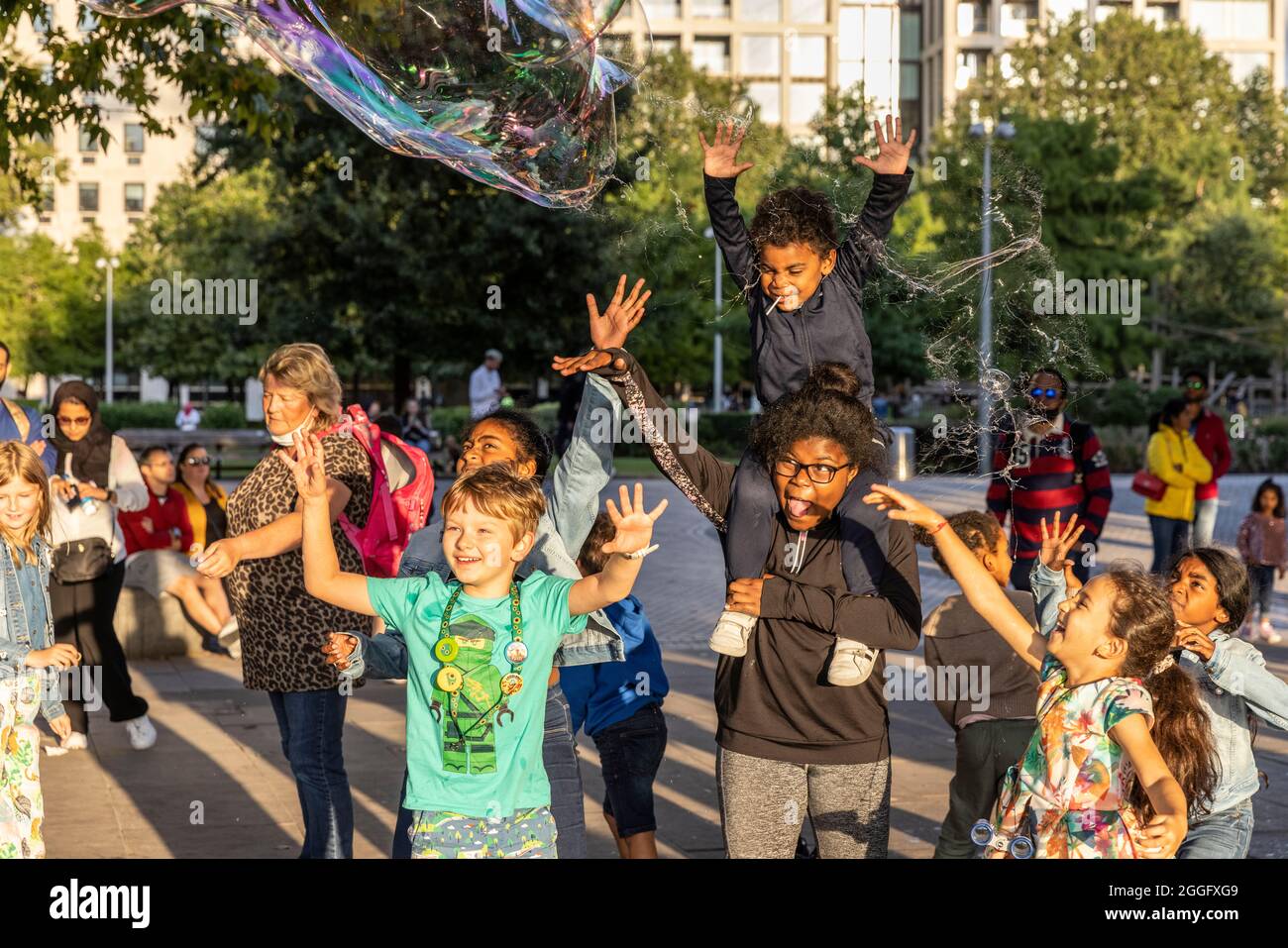 Les familles apprécient les divertissements de la rue le long de la Southbank à Londres tandis qu'un interprète souffle de grandes bulles à travers le pavé, Angleterre, Royaume-Uni. Banque D'Images