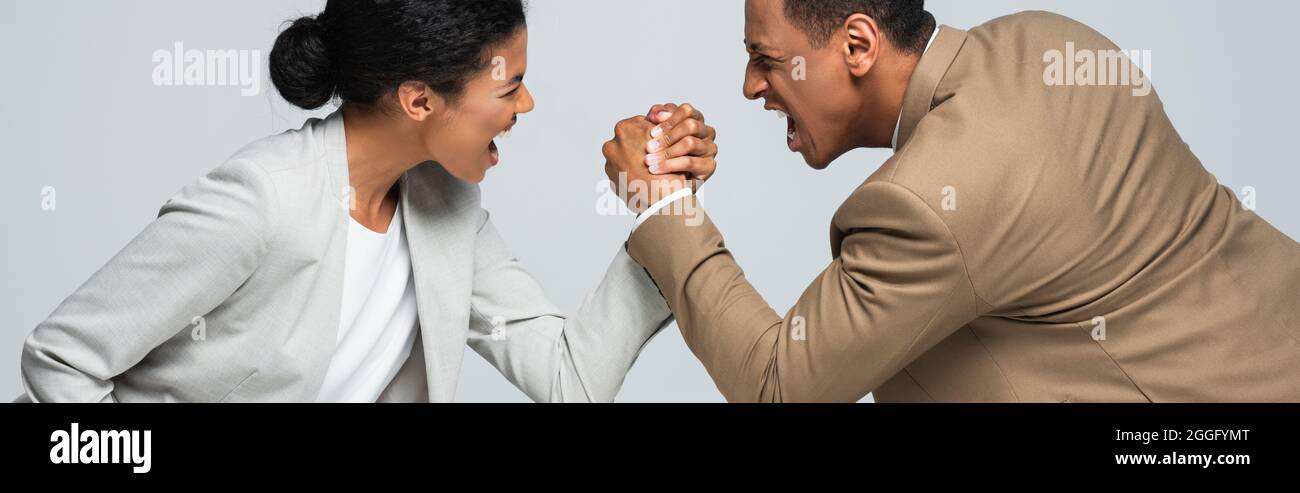 vue latérale de la femme d'affaires afro-américaine et de l'homme qui fait le bras lutte sur la chaise blanche isolée sur la bannière grise Banque D'Images