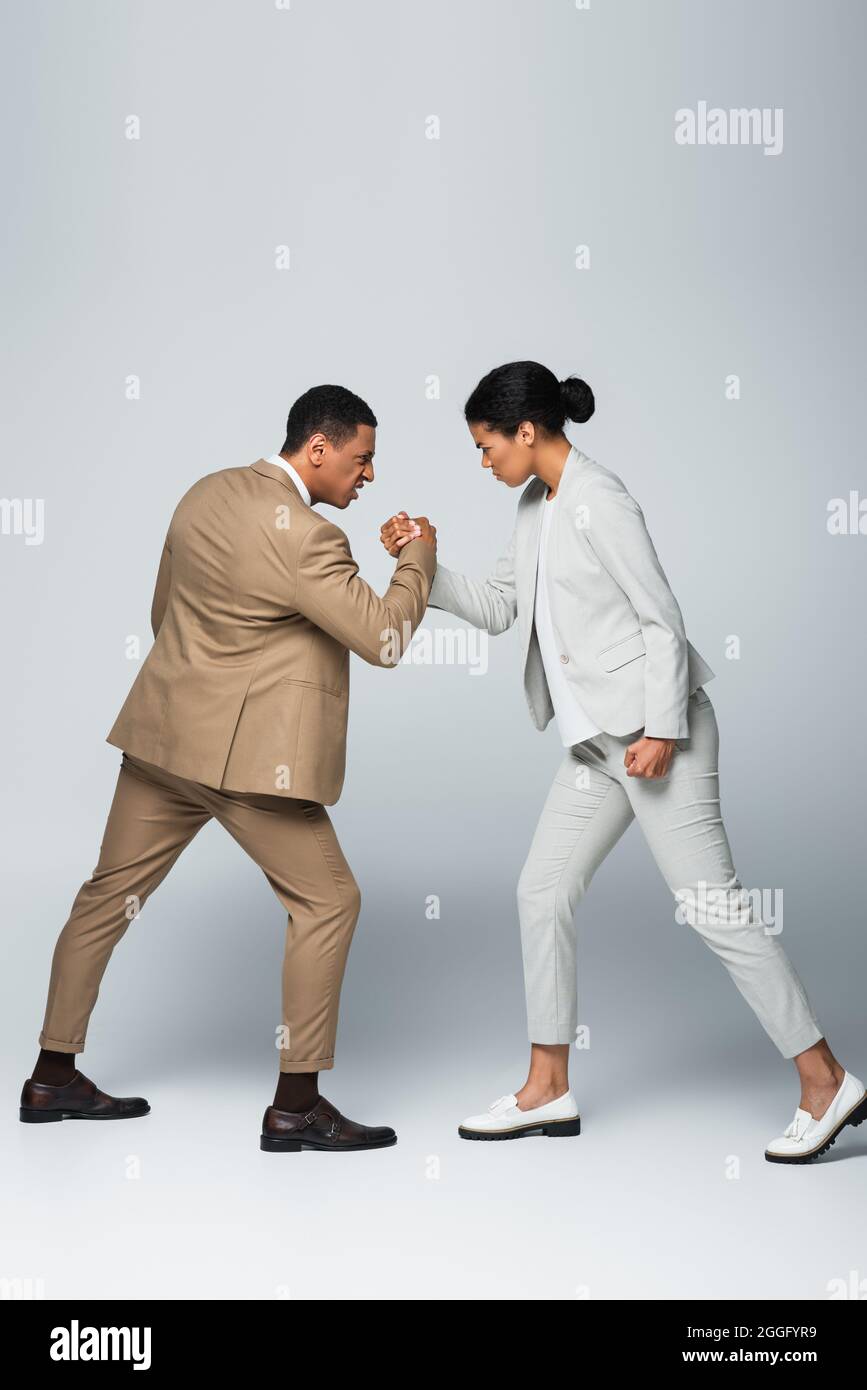 vue latérale de la femme d'affaires afro-américaine et de l'homme qui fait la lutte de bras sur le gris Banque D'Images