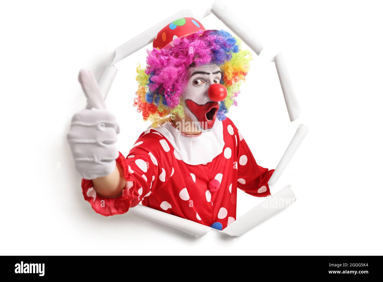 Un clown gai se pageant à travers un trou de papier et faisant des gestes de pouce vers le haut isolés sur fond blanc Banque D'Images