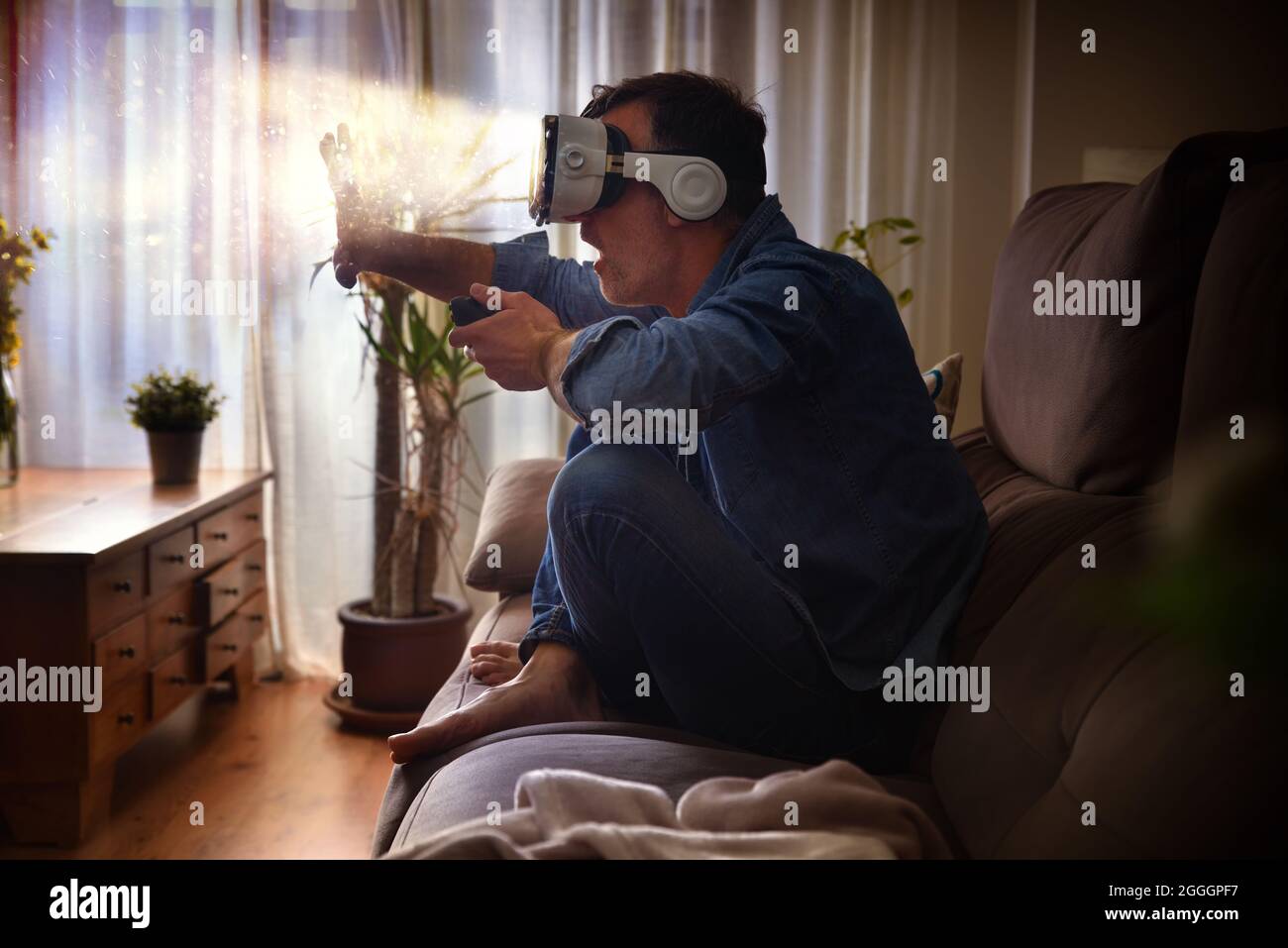 Concept d'homme en interaction avec des lunettes de réalité virtuelle avec contrôleur sur le canapé à la maison Banque D'Images