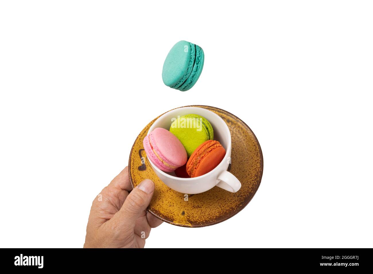 Des macarons colorés se levent sur une tasse de thé blanc avec une main tenant une soucoupe brun jaunâtre. Isolation sur fond blanc. Banque D'Images