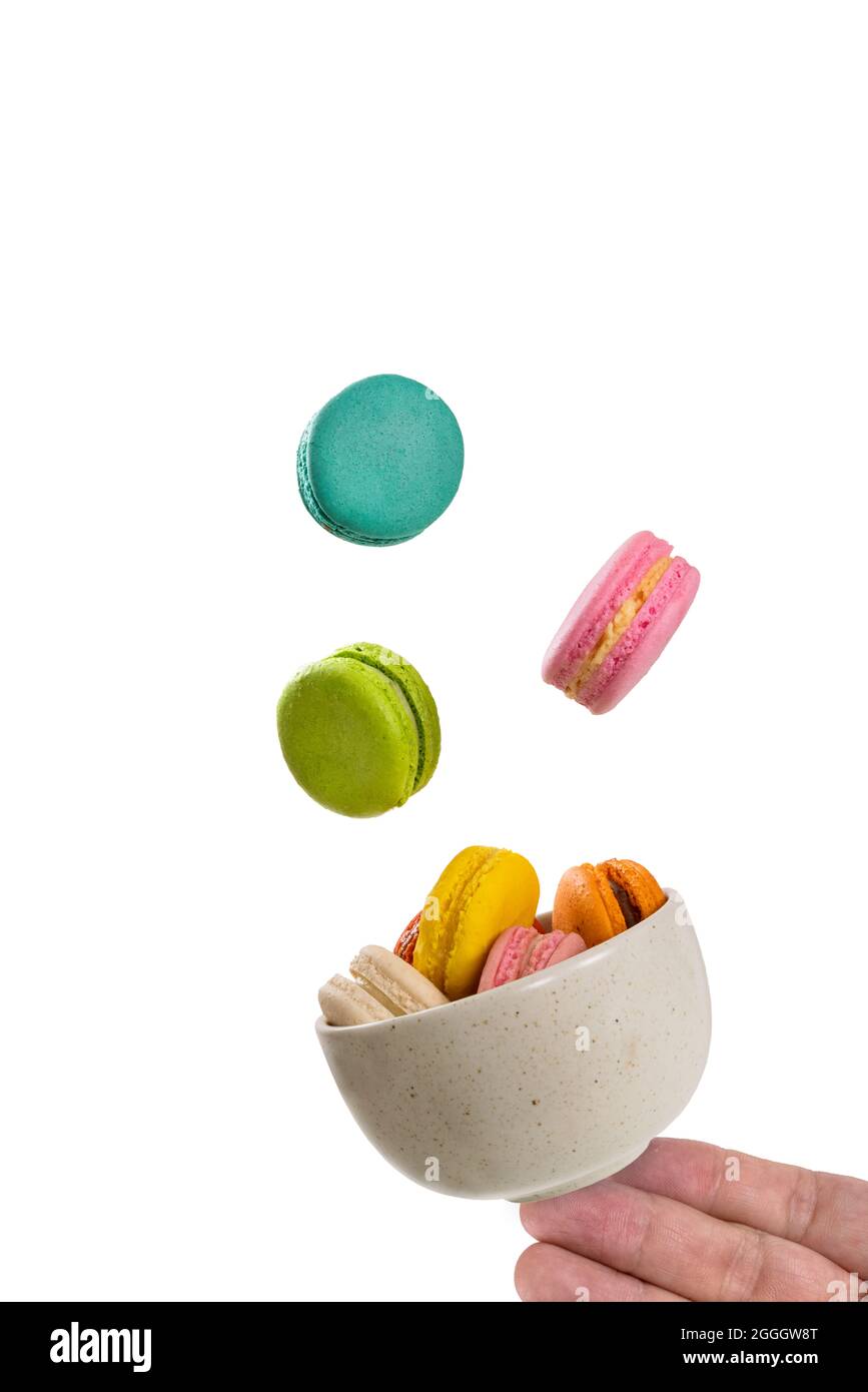 Macarons colorés flottant sur un bol en céramique avec une main tenant sa base avec des bouts de doigts. Isolation sur fond blanc. Concept de lévitation alimentaire. Banque D'Images