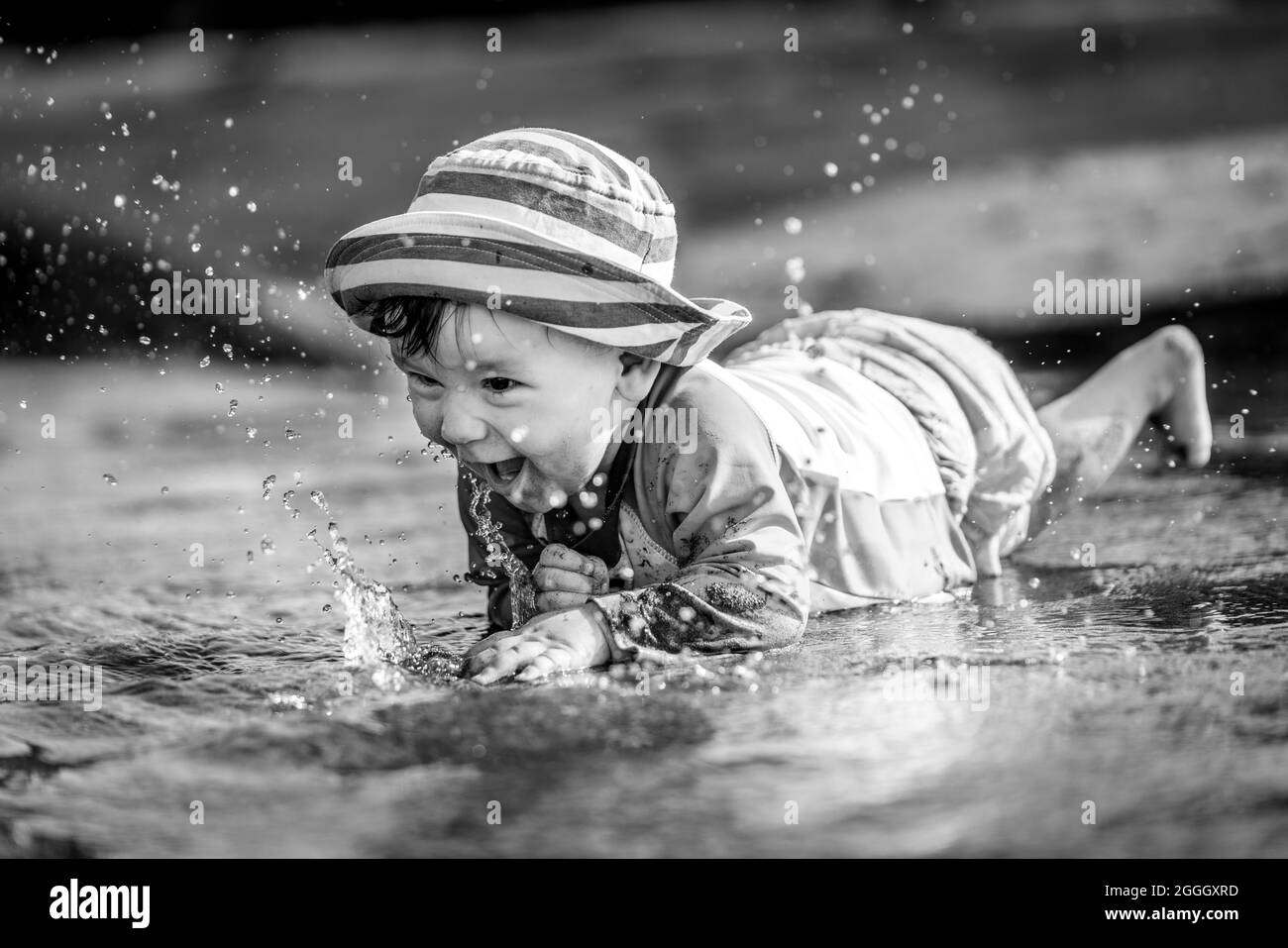 Photo en noir et blanc d'un tout-petit (petit garçon) qui rampe dans l'eau, rit et éclabousse de l'eau partout. Banque D'Images