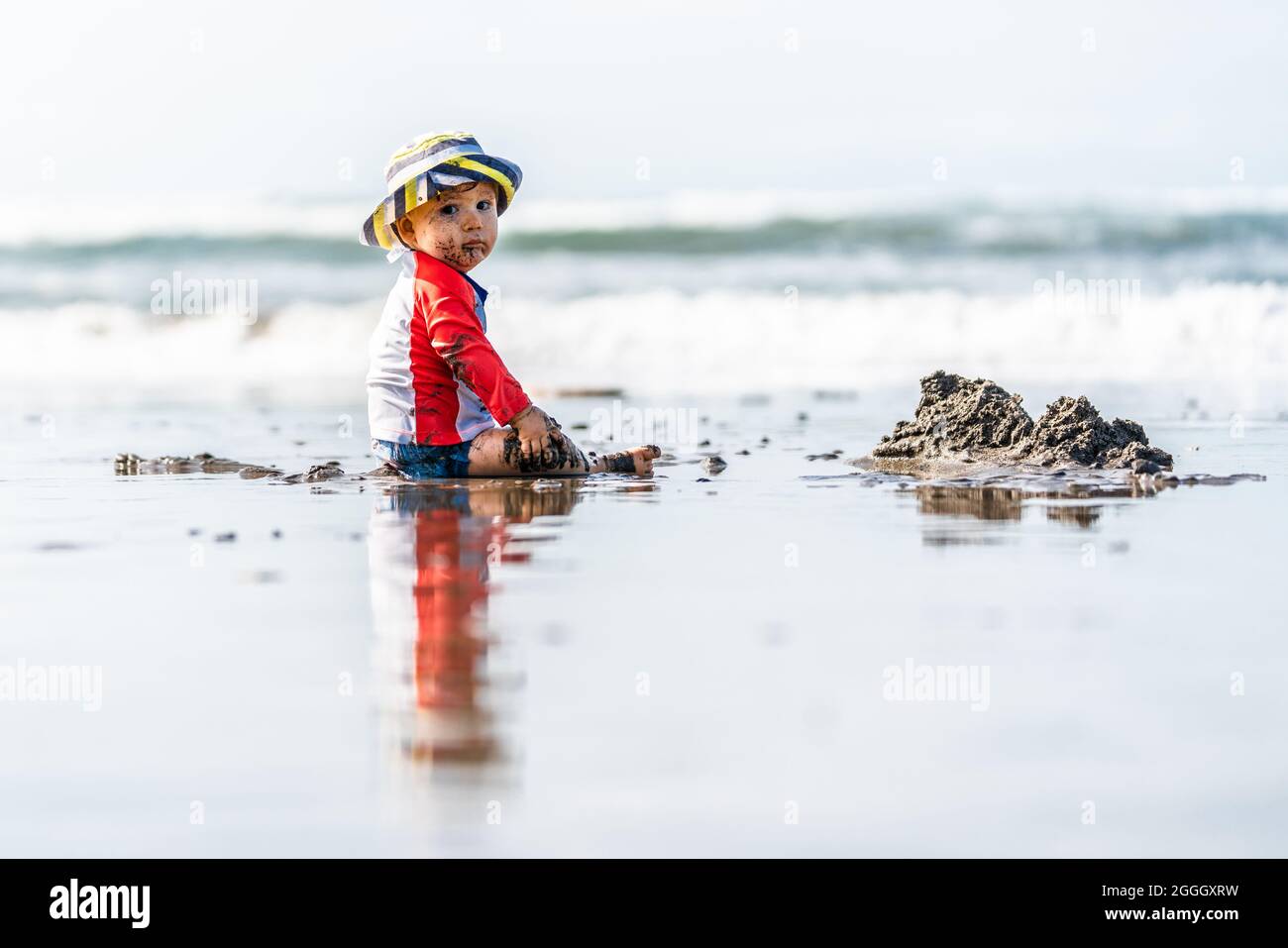 Beau bébé garçon assis à la plage et regardant dans l'appareil photo.Sur le  fond de l'horizon.L'enfant porte un chapeau rayé jaune Photo Stock - Alamy