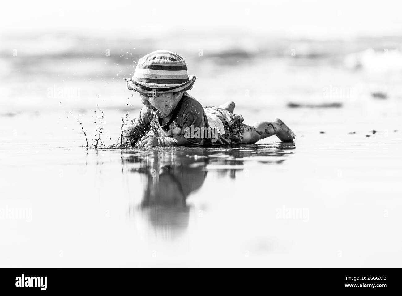 Une Photo En Noir Et Blanc D Un Beau Bebe Garcon Qui Eclabousse De L Eau Et Rampant Sur Une Plage L Enfant Porte Un Chapeau Raye Photo Stock Alamy