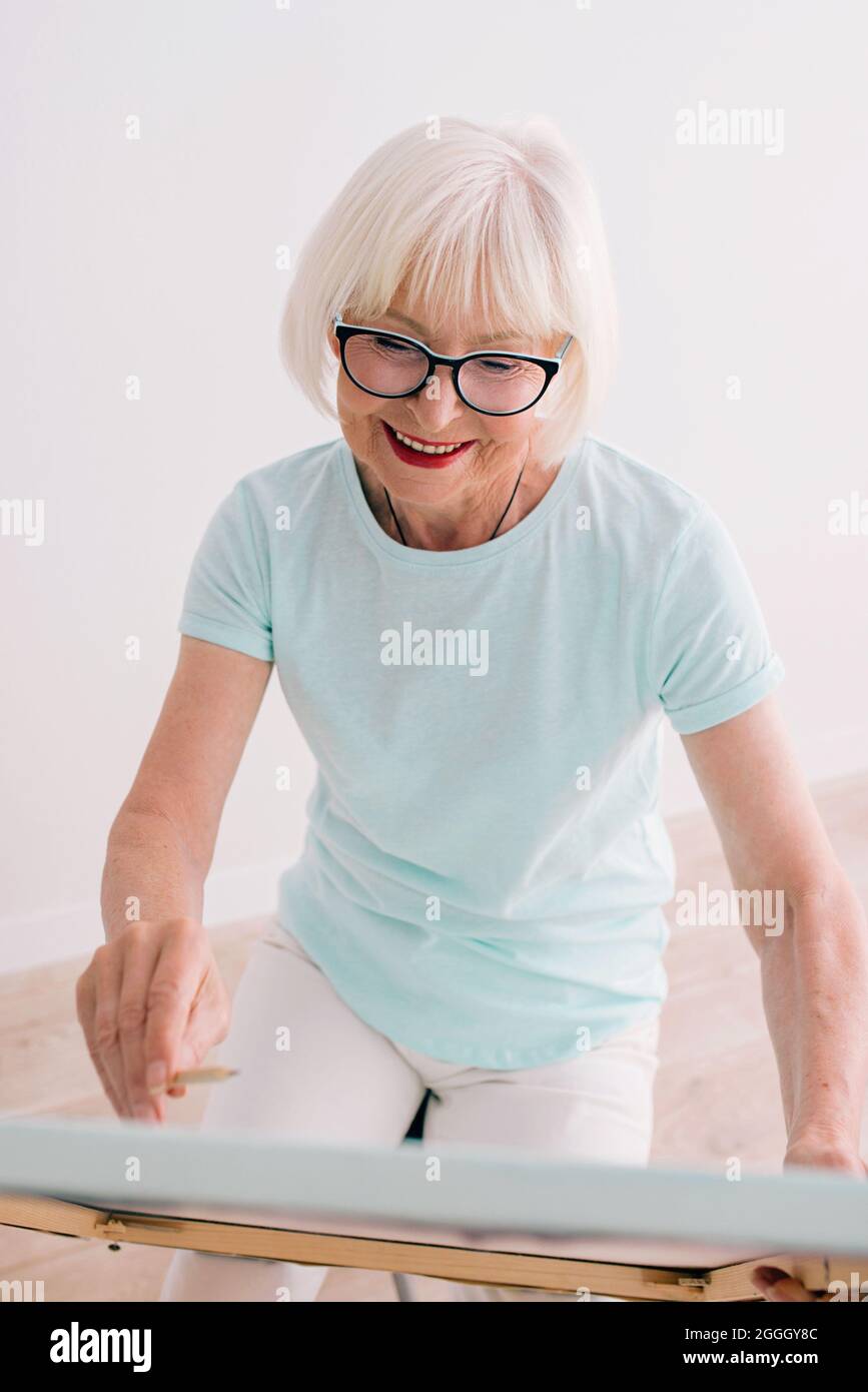 femme joyeuse senior en lunettes avec dessin de cheveux gris Banque D'Images