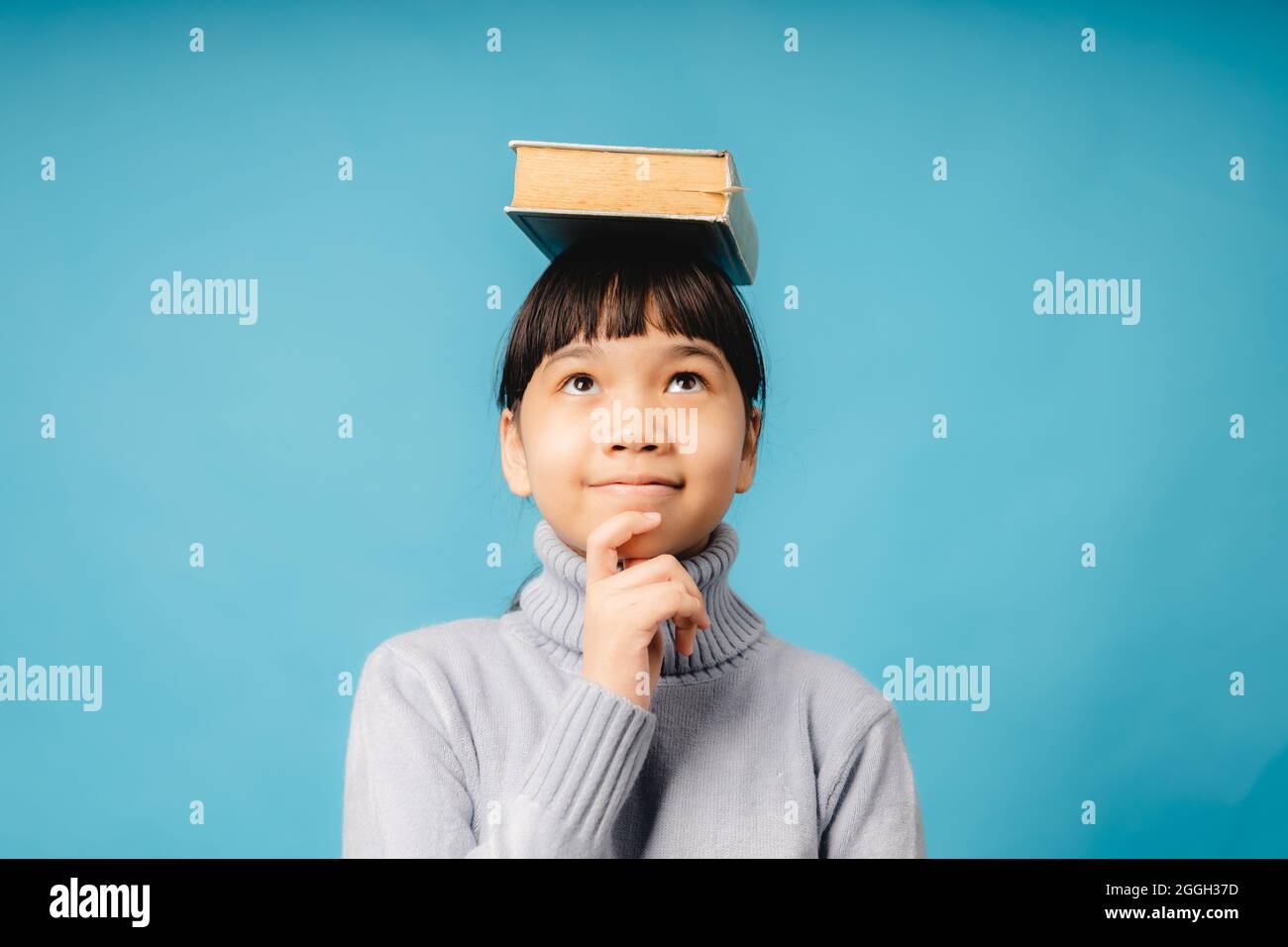Portrait de la jeune étudiante et fille asiatique a mis grand livre sur sa tête et de la pensée, l'idée et l'innovation éducative du concept d'enfant Banque D'Images