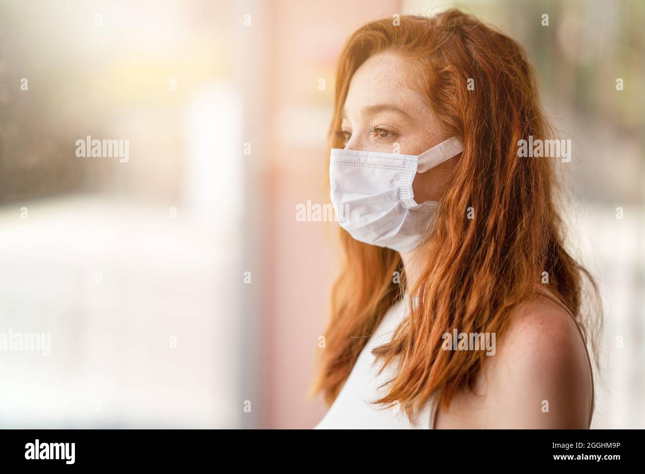 La jeune femme est debout et regarde de la fenêtre avec un masque de protection sur son visage. La rupture du virus Corona. Photo de haute qualité Banque D'Images