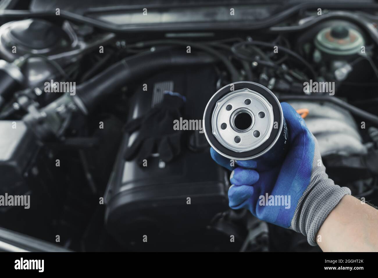 Remplacement du filtre à huile. Le mécanicien d'entretien de moteur de voiture tient un filtre à huile dans sa main contre le fond d'un capot de voiture ouvert Banque D'Images